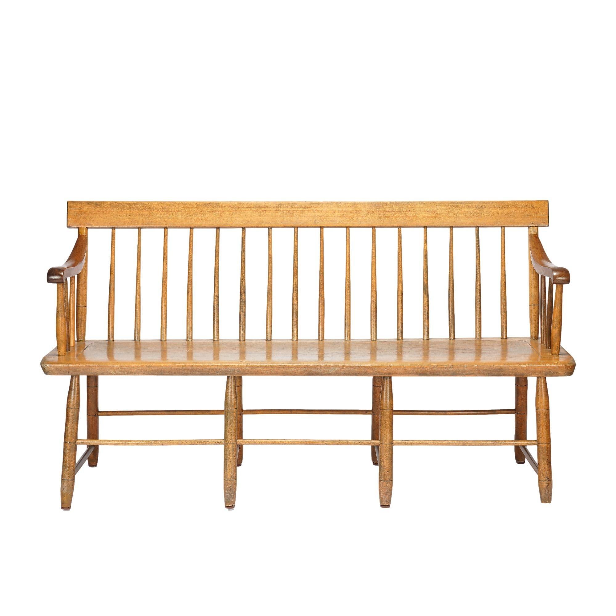 Windsor bench with carved mahogany arms and mixed woods. The bench has a birch crest rail supported by turned spindles on a single pine board shaped seat supported by bamboo turned legs with box stretchers. The arms are scroll carved mahogany and