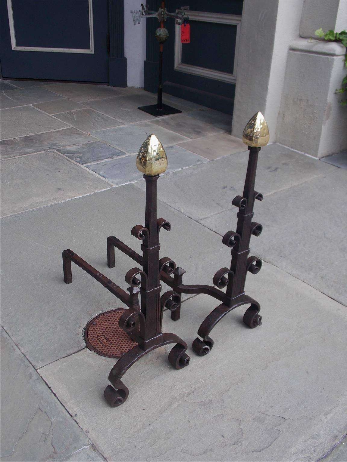 American wrought iron and brass andirons with faceted arrow finials, tapered squared plinths, artistic graduated scroll work, matching finial log stops, and terminating on decorative scrolled legs, Mid-19th century.