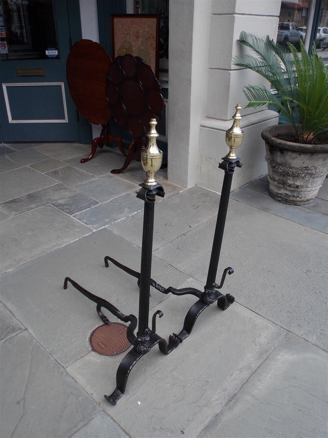 American wrought iron and brass urn finial andirons with upper scrolled decorative floral motif, fluted centered columns, flanking lower spit hooks, and resting on the original scrolled stylized paw feet. Andirons have the original stylized snake