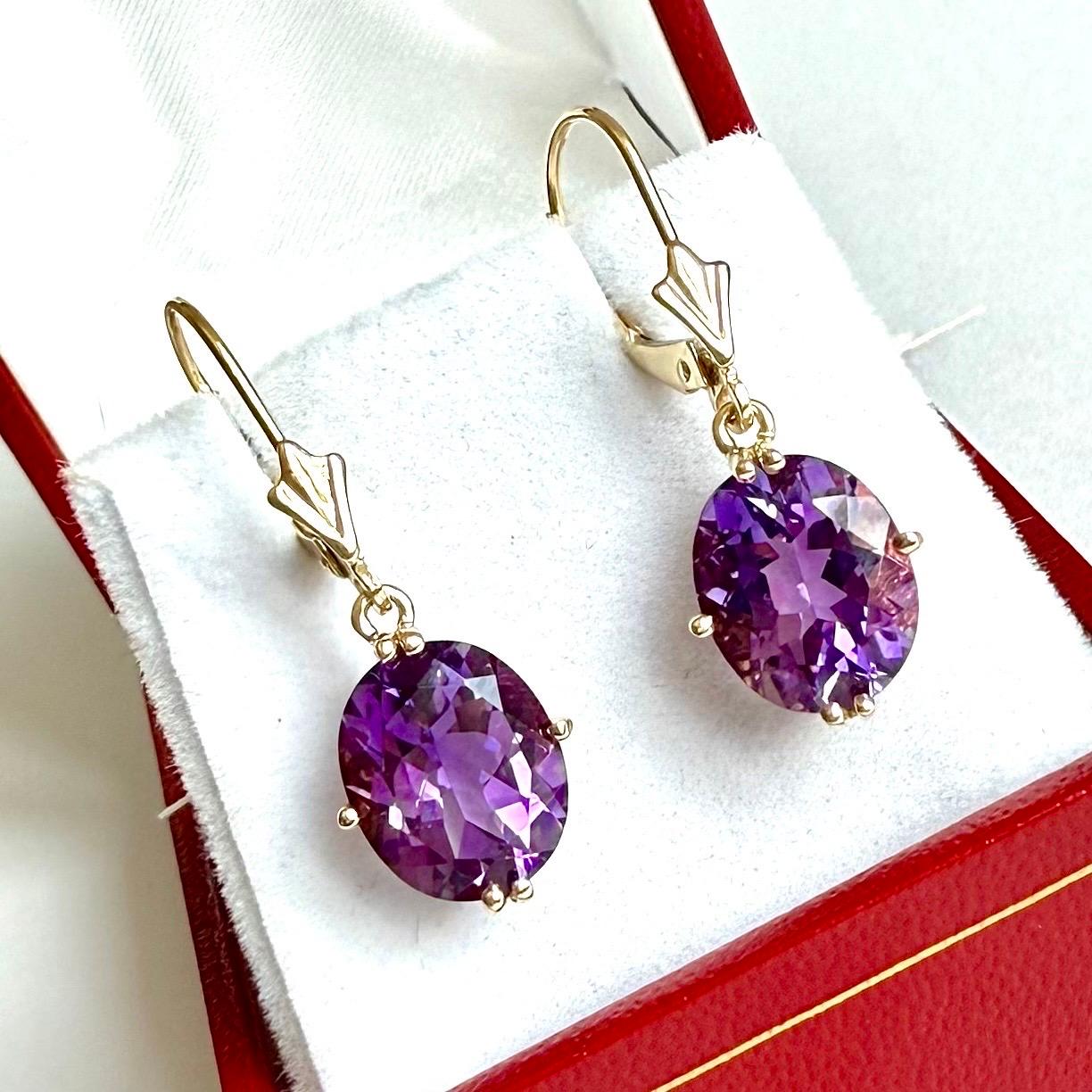 Magníficos pendientes de oro amarillo de 14k con una piedra amatista de talla ovalada, en excelente estado. Los pendientes tienen un cierre de palanca y un diseño sencillo y elegante. El oro tiene un tono cálido y brillante, y la amatista es de un