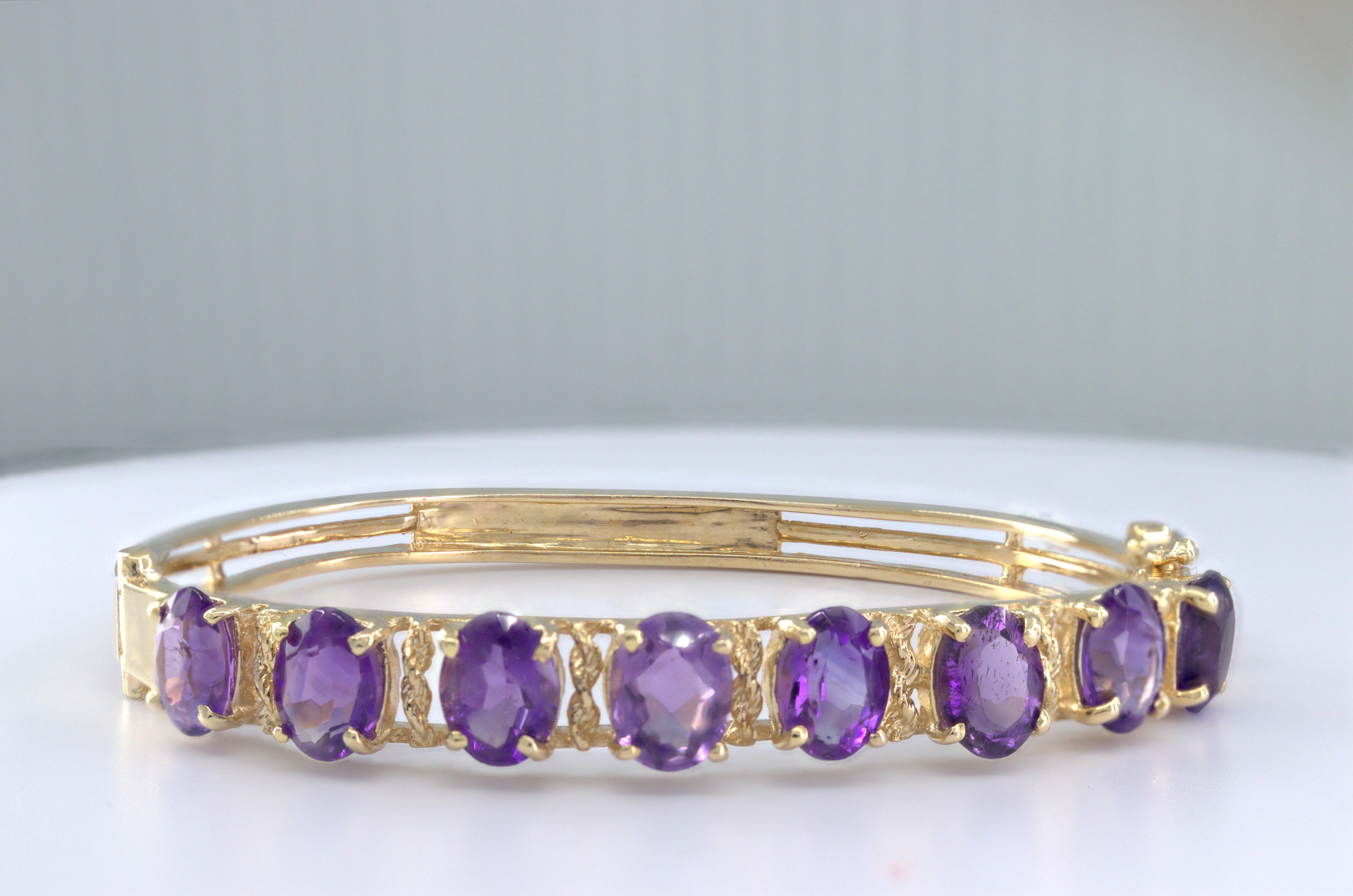 Featuring (8) oval-cut amethysts, 8.15 cts. tw., set in a 14k yellow gold rope twist, hinged bangle mounting, with a tongue and groove clasp and figure eight safety, tapering from 6.9 mm to 3.9 mm, 54.2 mm widest internal diameter, Gross weight
