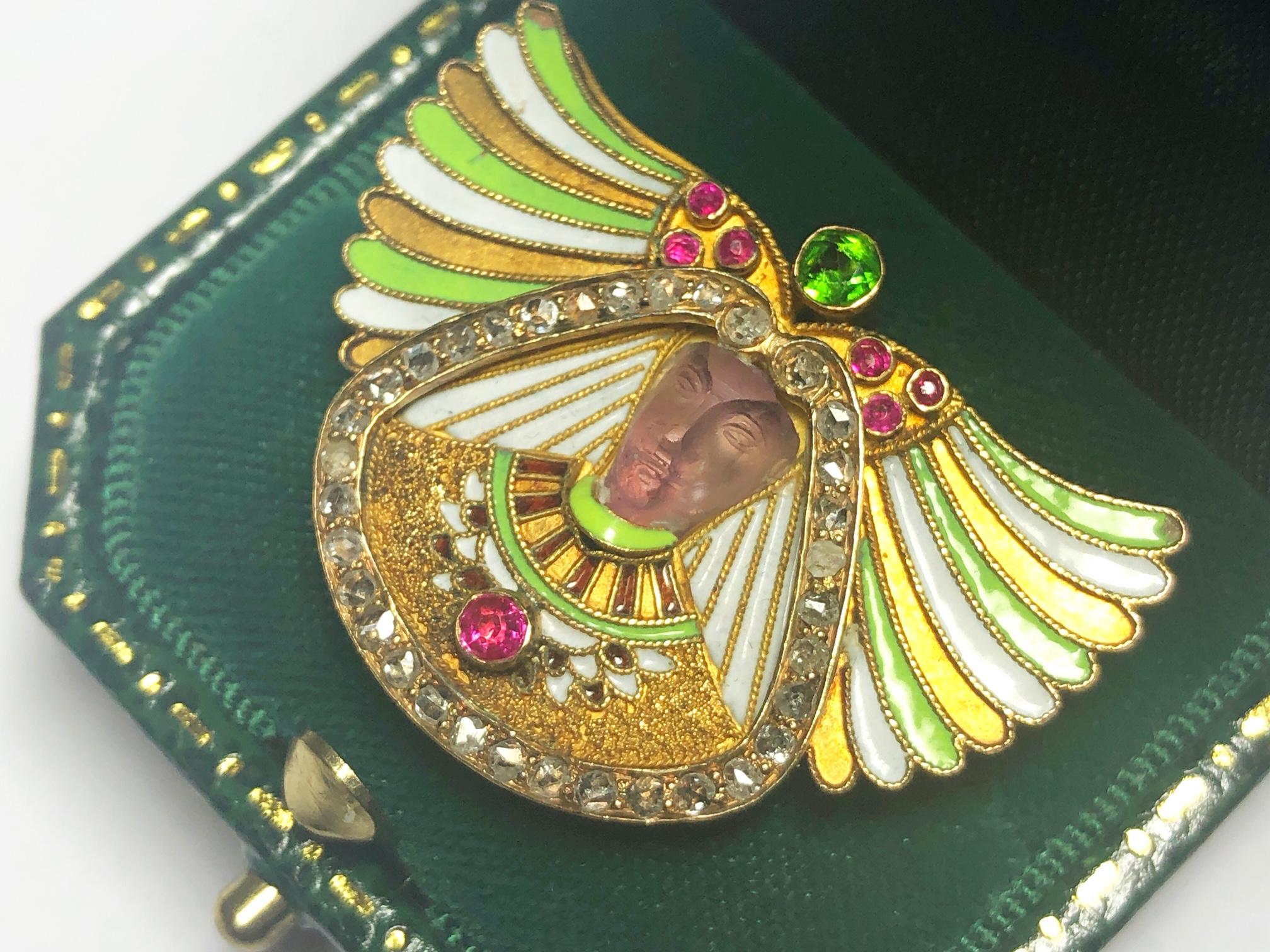 An Austro-Hungarian, Egyptian Revival, pharoah's head, gem-set brooch, with a carved amethyst head, wearing a Nemes headdress, in green and white, cloisonné enamel, with twisted wire edging, topped by round faceted rubies and a demantoid garnet, in