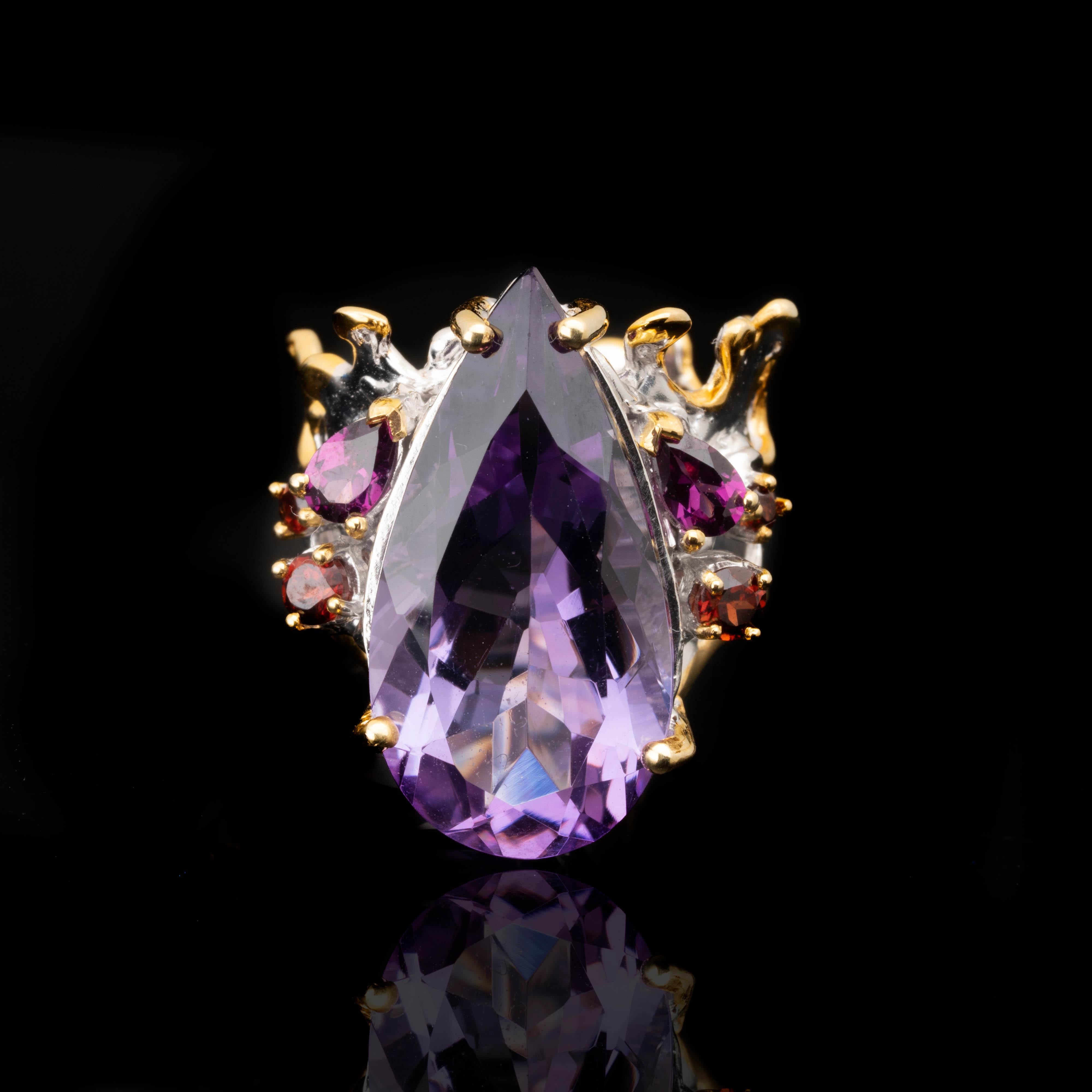 This royally decadent ring features a large, incredibly clear, sparkling teardrop amethyst adorned with rhodolites and garnets in a sterling silver setting with luxe 14k gold accents and crown-like detailing. An accessory fit for a