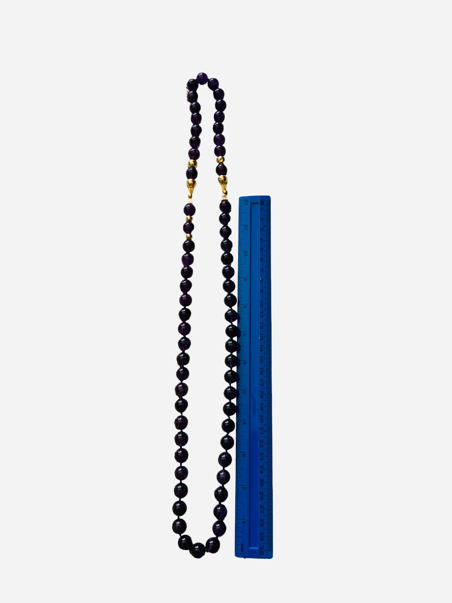 This is an Amethyst and gold beads long necklace. It depicts a necklace made of round large amethyst spheres fasten on a string. It is adorned with large gold beads and ribbed small “trumpets” that are also placed in the same way. Amethyst beads