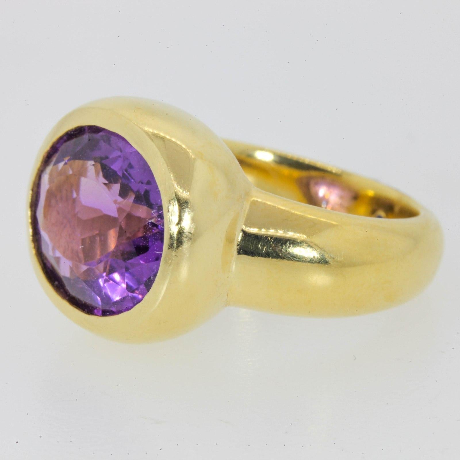 Luminous & Fashionable!  A contemporary 18KT yellow gold ring featuring a large oval cut bezel set Amethyst.  The tapered band is accented on the outside with a 0.01 carat blue Sapphire.  The ring is size 6 3/4.  