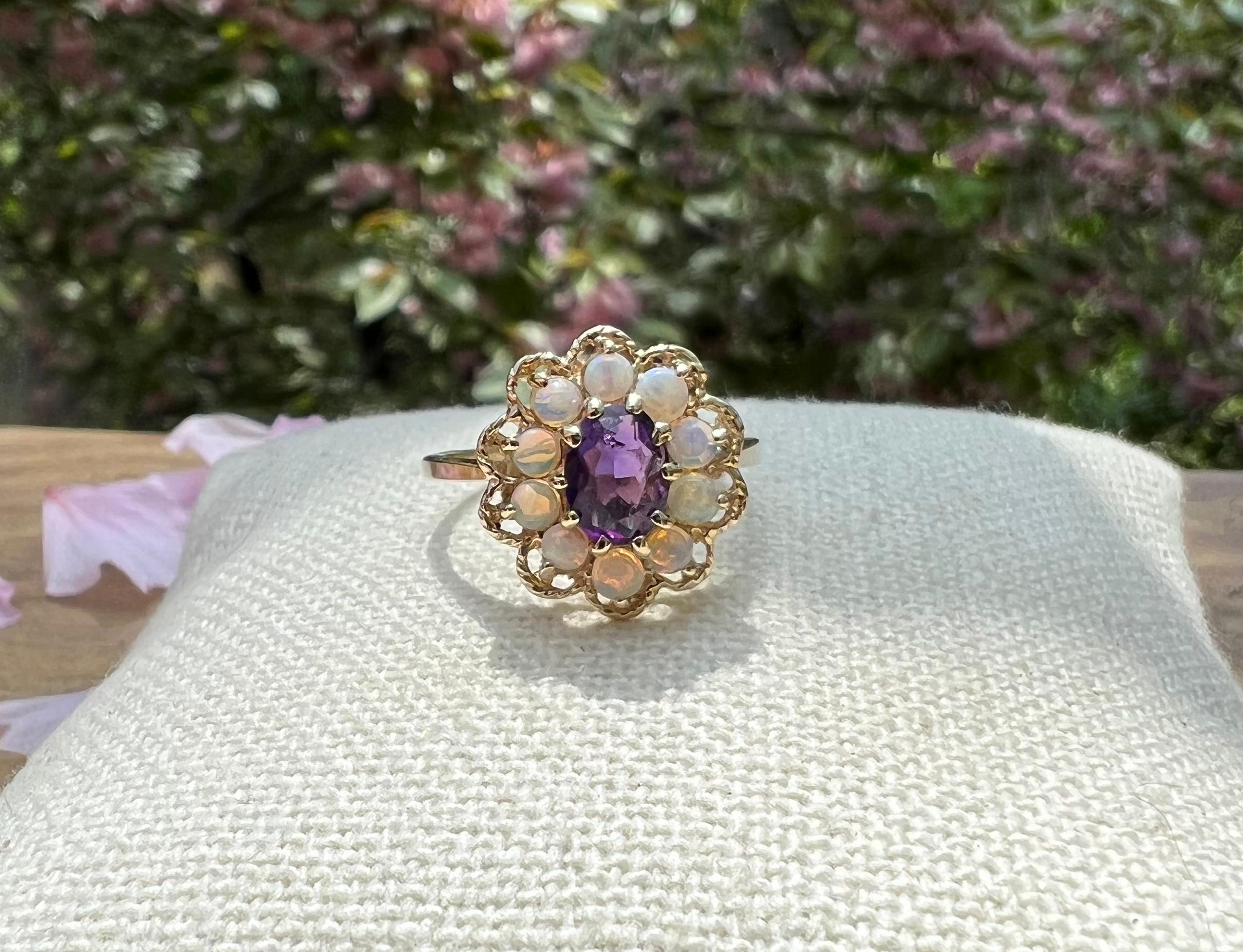 One 14-karat yellow gold (stamped 14K) ring set with one 7 x 5mm oval amethyst surrounded by a halo of 2.5mm round opals.  The ring is a finger size 7.5.