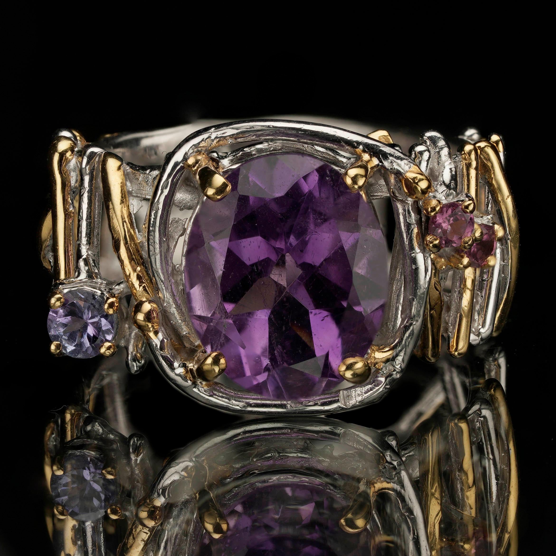 Dieser atemberaubende Cocktailring aus Amethyst und Rhodolith ist eine faszinierende Verschmelzung von Farbe und Design. Ein facettierter Amethyst in der Mitte des Rings mit satten, violetten Farbtönen, flankiert von funkelnden Rhodolithen, macht