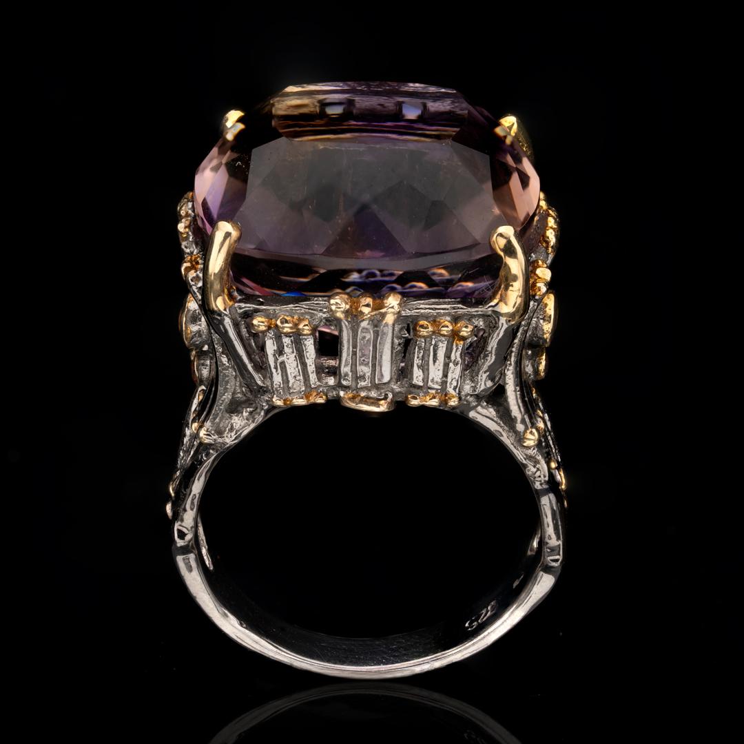 This large and flawless deep purple natural amethyst has been square-cut and placed in a uniquely and intricately hand-carved rhodium plated sterling silver prong setting and band both tastefully ornamented with luxe gold leaf. One round pink and