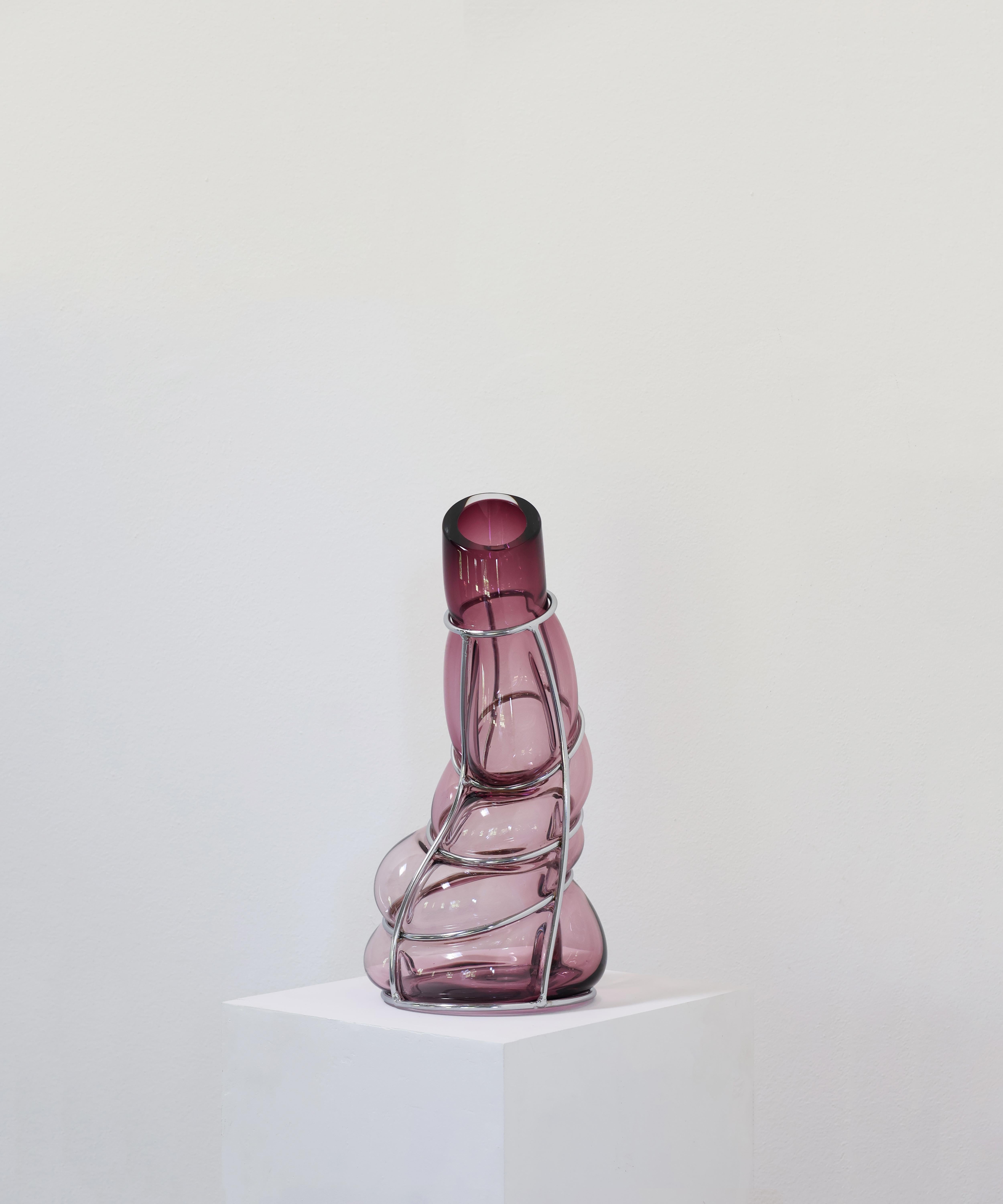 Vaso scultoreo Ametista Babà di Alice Crepaldi
Un pezzo unico.
Dimensioni: Ø 20 x H. 40 cm.
Materiali: Vetro di Murano e metallo.

Adornato da uno stelo leggermente più corto ma elegante, questo vaso ingabbiato utilizza la tecnica dello 