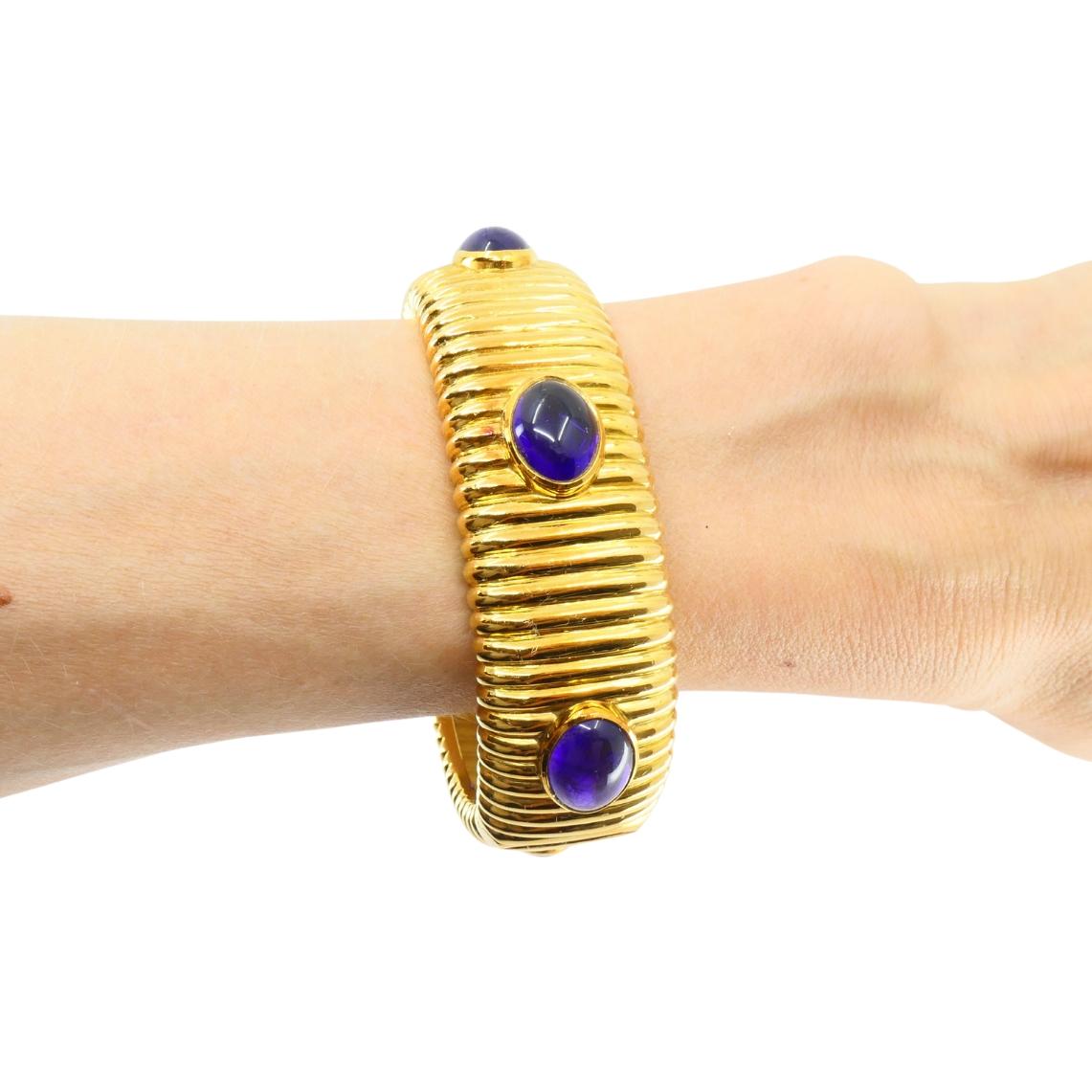 Questo bracciale vintage di Tambetti è realizzato in oro giallo 18 carati con ametiste ovali tagliate a cabochon. Il bracciale presenta una superficie rigata che corre verticalmente intorno all'intera banda. Sei ametiste sono distribuite