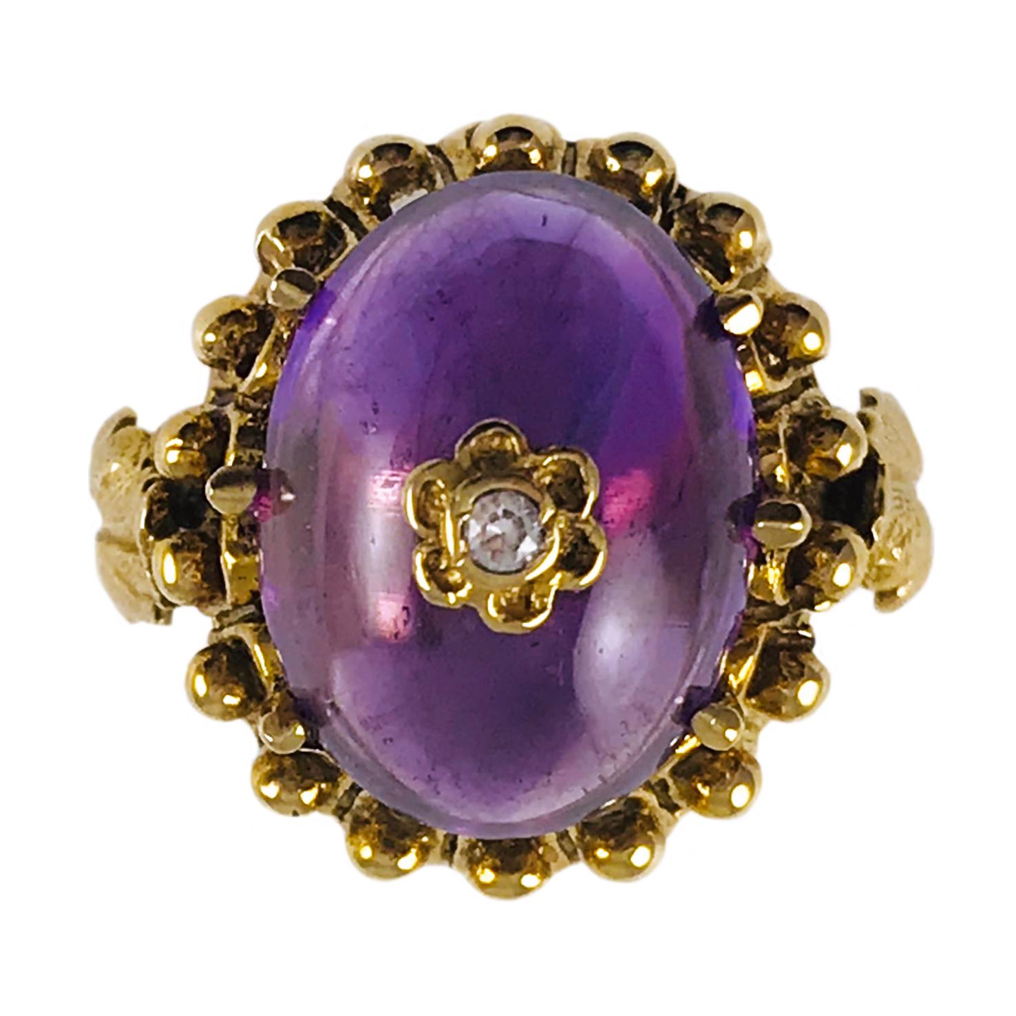 14 Karat Yellow Gold Amethyst Diamond Ring. The Amethyst Cabochon measures 16 x 13mm and is six-prong set. Six small gold petals form a flower at the center of the cabochon with the center of the flower featuring a bezel-set round diamond. The ring