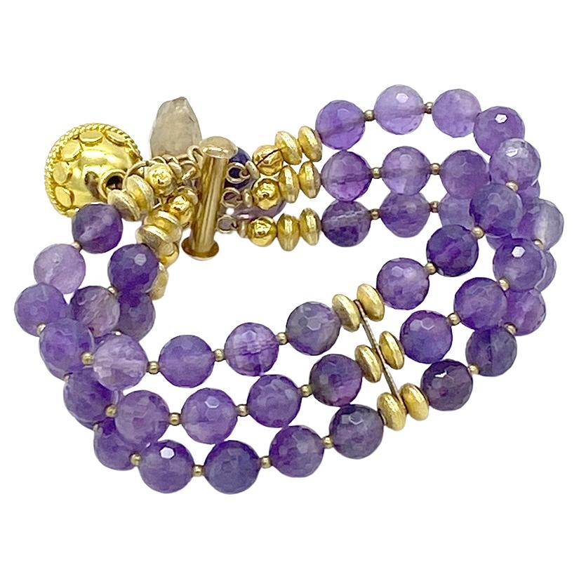 Questo è un braccialetto di charme in ametista. Abbiamo creato questo bracciale triplo con perle di ametista semitrasparente sfaccettate da 8 mm e componenti placcati in oro. Presenta una perla decoreata Bali da 16 mm e un grappolo di perline