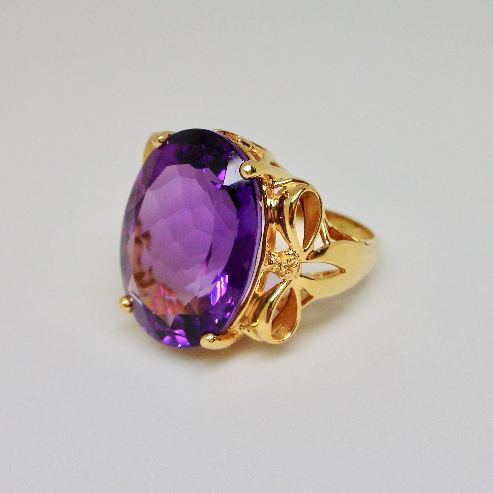 Unsual cocktail ring from the 1960s set in 14ct gold with bow designs on the side, centering with an intense oval cut natural amethyst of 20 carats circa. 

Italian Ring size: 12.5 (Can be resized)