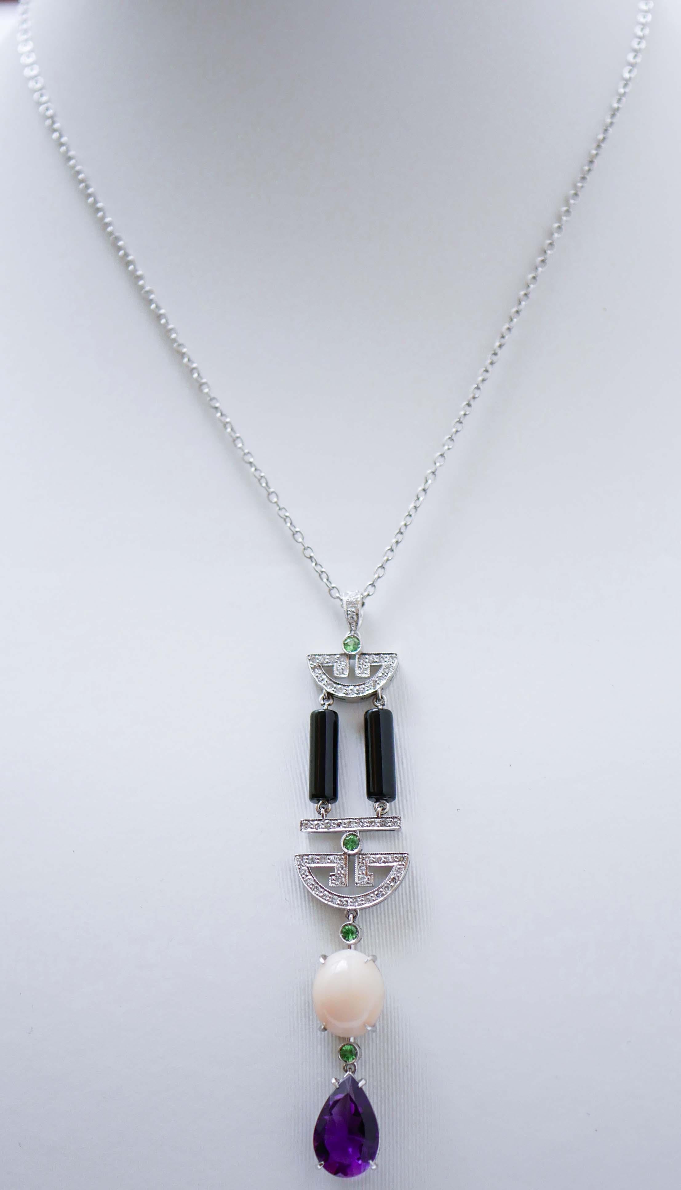 Fantastica collana con ciondolo in oro bianco 18 kt, montata con diamanti e tsavorite nella parte superiore; in  al centro, onice, diamanti e tsavorite; nella parte finale, un corallo e un'ametista a goccia uniti dalla tsavorite.
La catena è