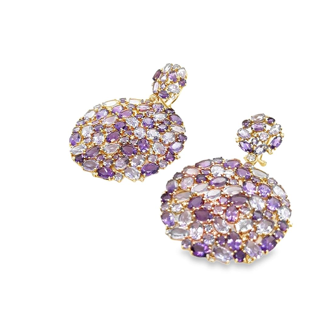 Beautiful pair of earrings crafted in 18k yellow gold. The pair highlight vibrant colored Amethyst gemstones adorned with diamonds in a scattered pattern. The earrings show a wide circular shape as they measures 1.5