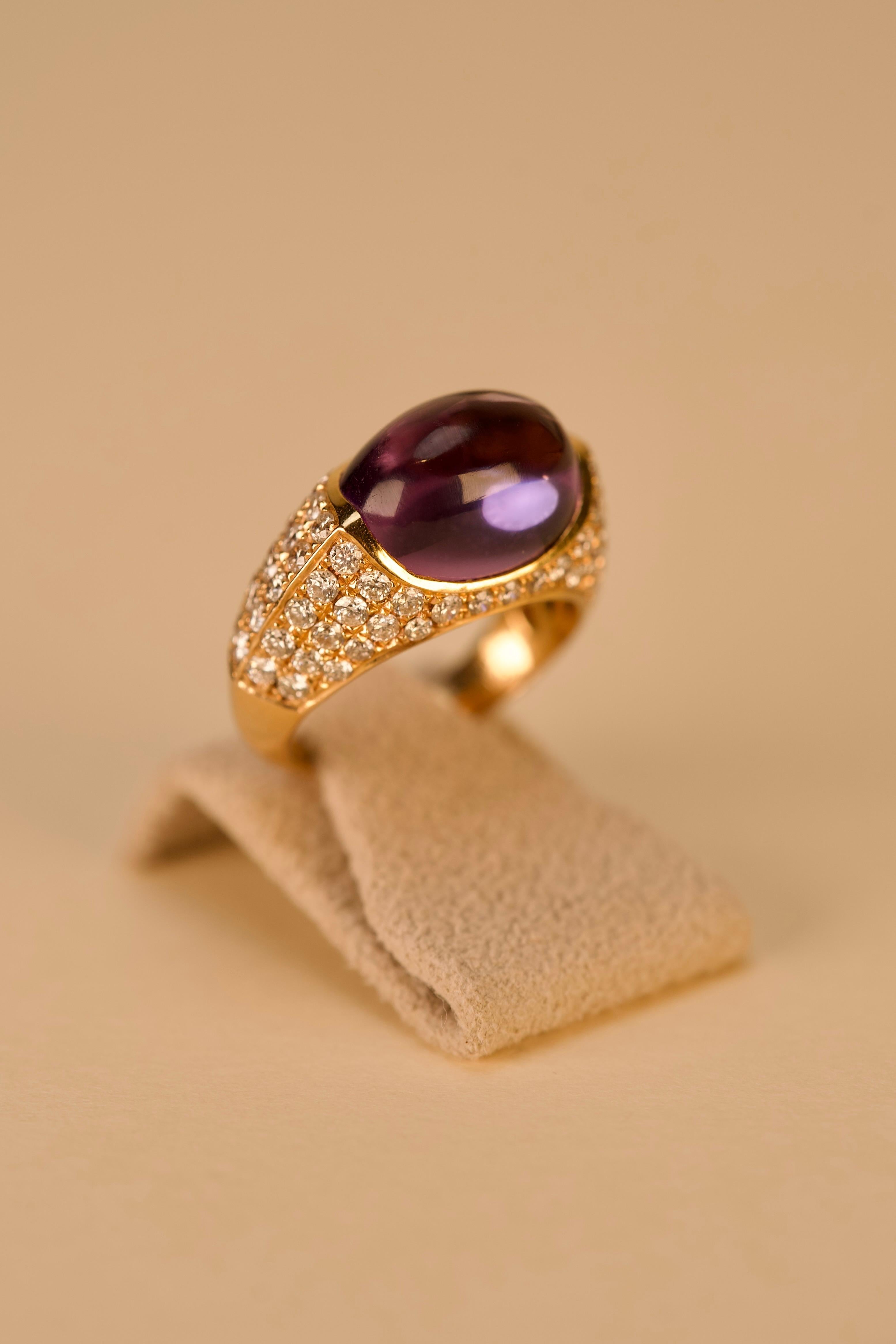 Cette bague cocktail améthyste-diamant en or est réalisée en or rose dix-huit carats et conçue avec un jeu captivant de couleurs et de lumière. Au centre repose une améthyste cabochon lisse, choisie pour sa riche teinte veloutée et sa douce surface