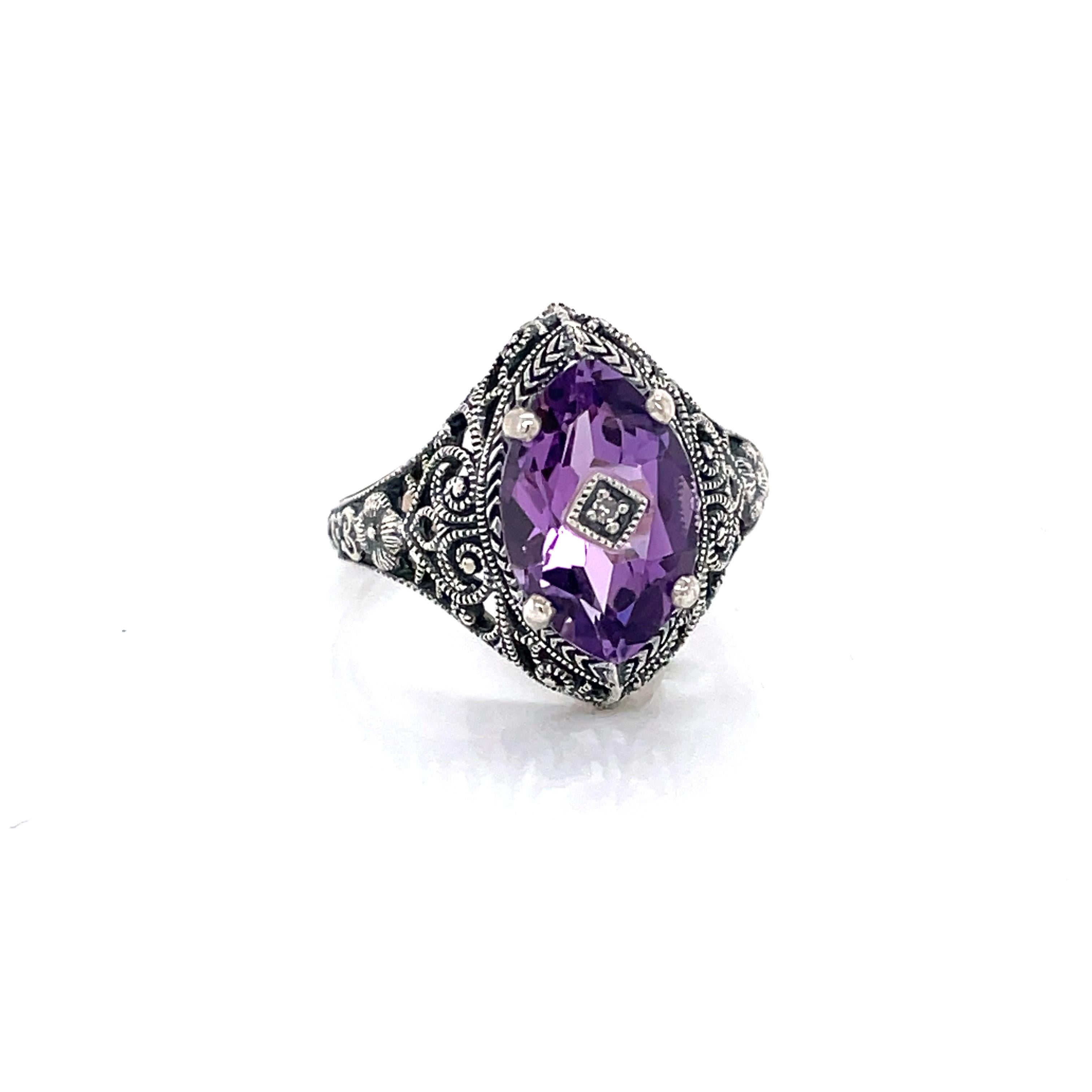  In Victorian style, the regal hue of this purple oval faceted amethyst catches the eye. A center diamond accent detail compliments the intricate filigree in .925 sterling silver.
In ring size 8. New and presented in an antique style gift box.   