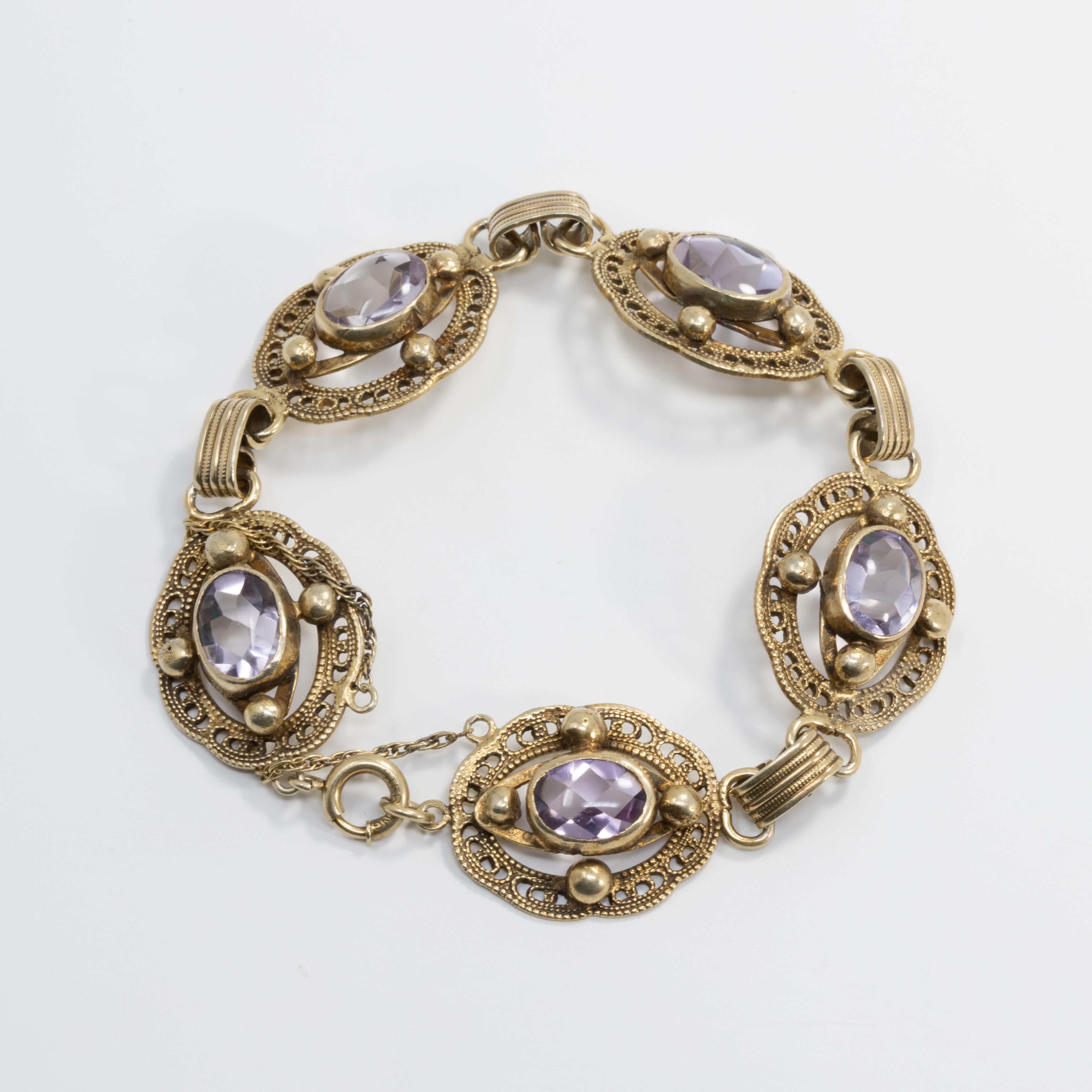 Un élégant bracelet vintage. Cet accessoire élégant comporte cinq maillons, chacun avec une améthyste unique sertie dans un cadre métallique décoratif. Fermeture avec un fermoir à ressort et une chaîne de sécurité. Poinçonné en tant que sterling.