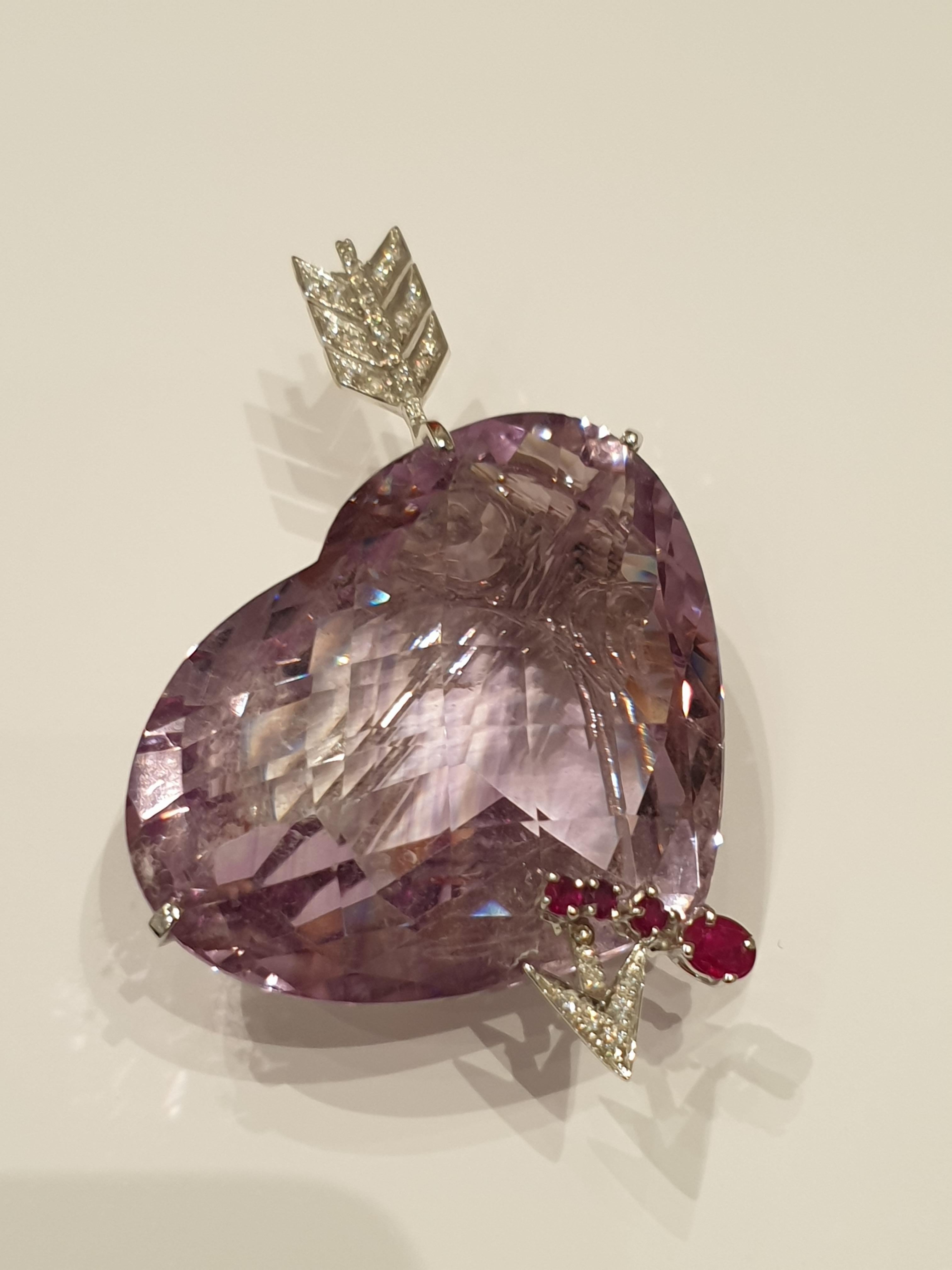 Heart shaped amethyst, untreated weighing 160 carats. 27 brillant-cut diamonds formed as an arrow, with a total weight of ca. 0.46 ct. Embellished with 4 rubies total weighing ca. 0,40 ct. Mounted in 18 K white gold. On the needle marked  with the