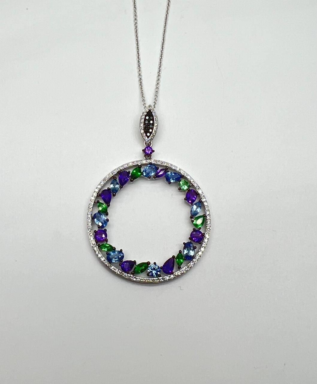 Questo straordinario design di collana con ciondolo è caratterizzato da un ciondolo circolare ornato da gemme vibranti nei toni del viola, del blu e del verde. Ogni pietra è incastonata in una delicata montatura, creando una composizione colorata e