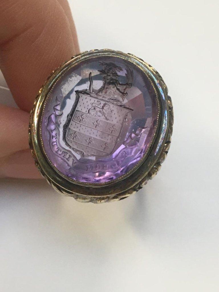 The oval amethyst, carved to depict a crest, with floral embossed gallery. Approximate ring size 7. Weight 15.7gms. 
Length of ring head 2.4cms.