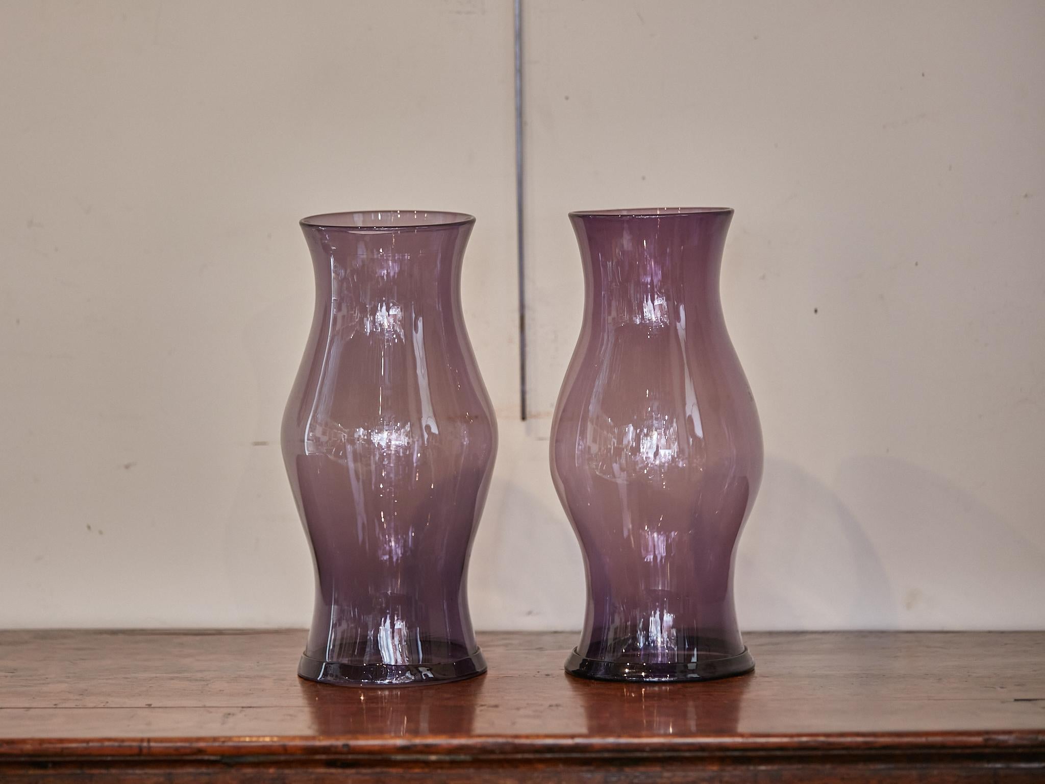 A pair of Midcentury American Amethyst color glass hurricane lamp shades. Evoke a sense of Midcentury magic in your home with this exquisite pair of American Amethyst-colored glass hurricane lamp shades. Radiating with a rich purple hue reminiscent