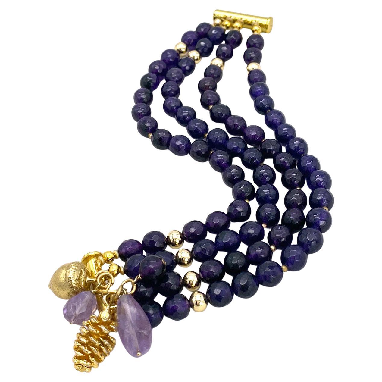 Il s'agit d'un bracelet à breloques multiples en améthyste. Nous avons créé ce bracelet avec des perles d'améthyste de 8 mm à facettes d'un violet profond, contrastées par des éléments plaqués or 14K. Il comporte des charmes en forme de gland, de