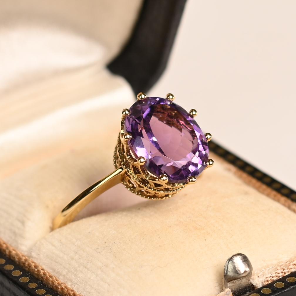 Este exquisito anillo de estilo antiguo exhibe una impresionante piedra central de amatista natural, con un peso aproximado de 3,30 quilates. El matiz profundo y real de la amatista se complementa maravillosamente con su experto facetado, que realza