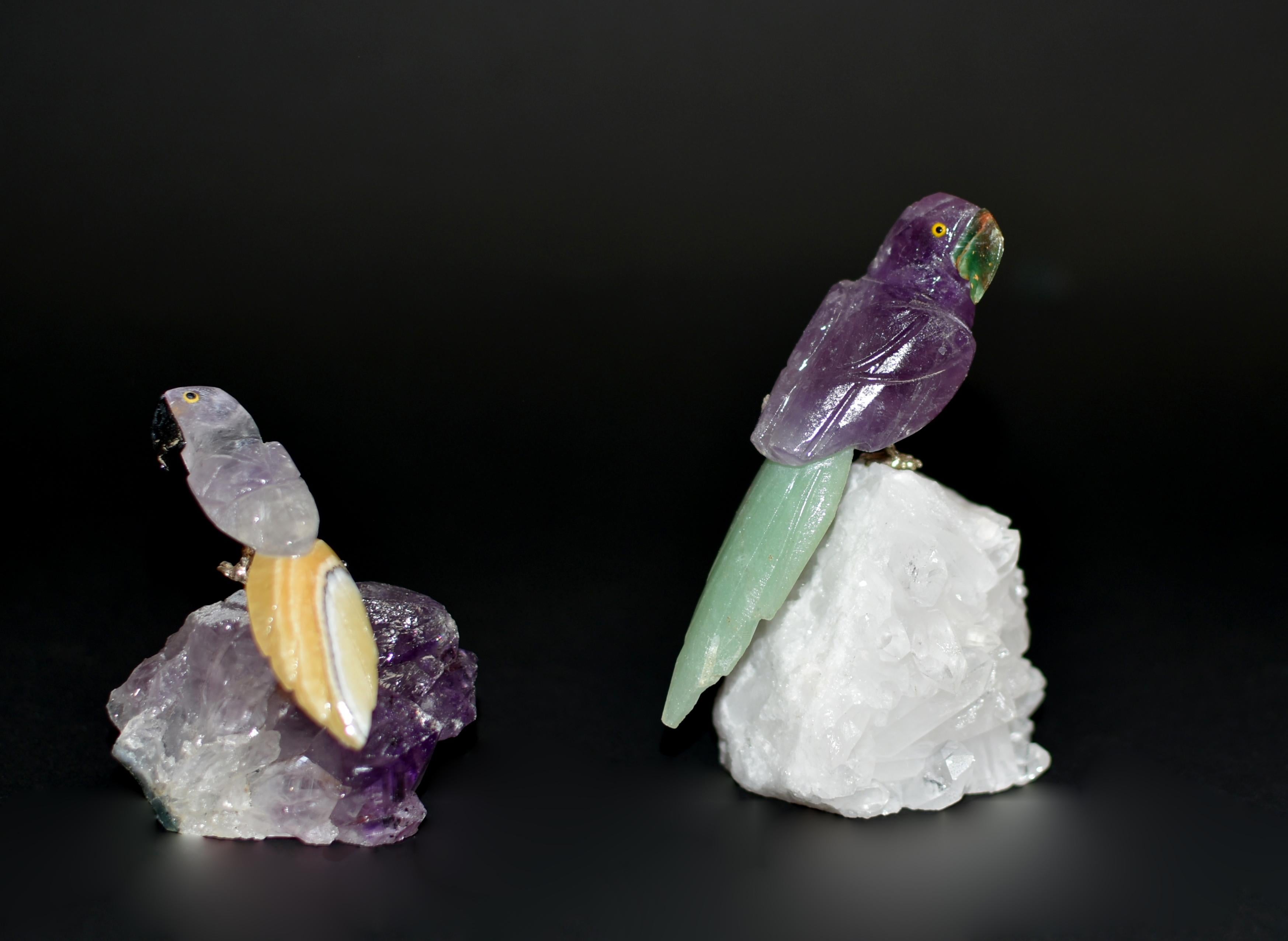 Two amethyst parrots perched on rock crystal and amethyst cluster. Realistically modelled with curious and alert expression, with natural purple amethyst plumage and tail in green aventurine and yellow calcite. Beaks in aventurine and black onyx.
