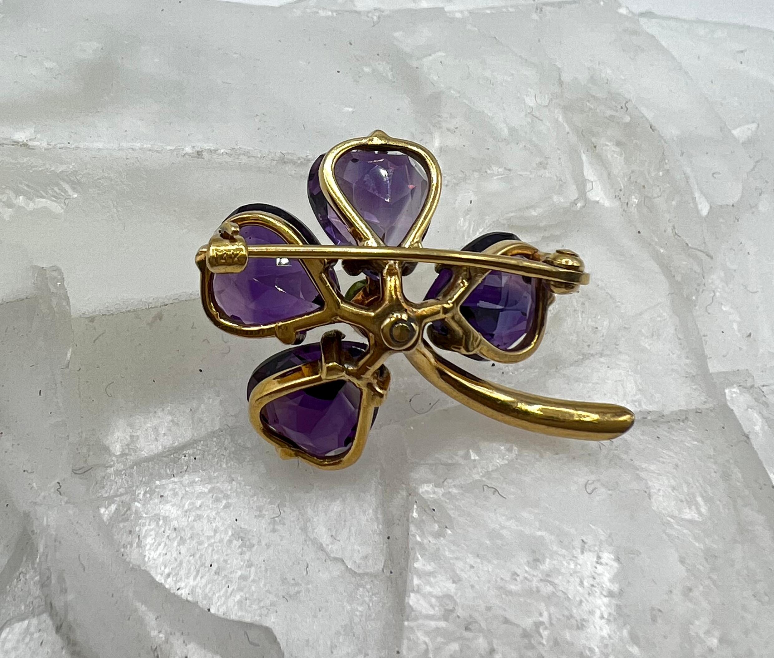 This sweet brooch is a lovely addition to a flora collection of jewels. The center green demantoid garnet is offset by beautifully faceted amethyst petals. The entire floral setting is 18 karat yellow gold for a beautiful contrast. This is a