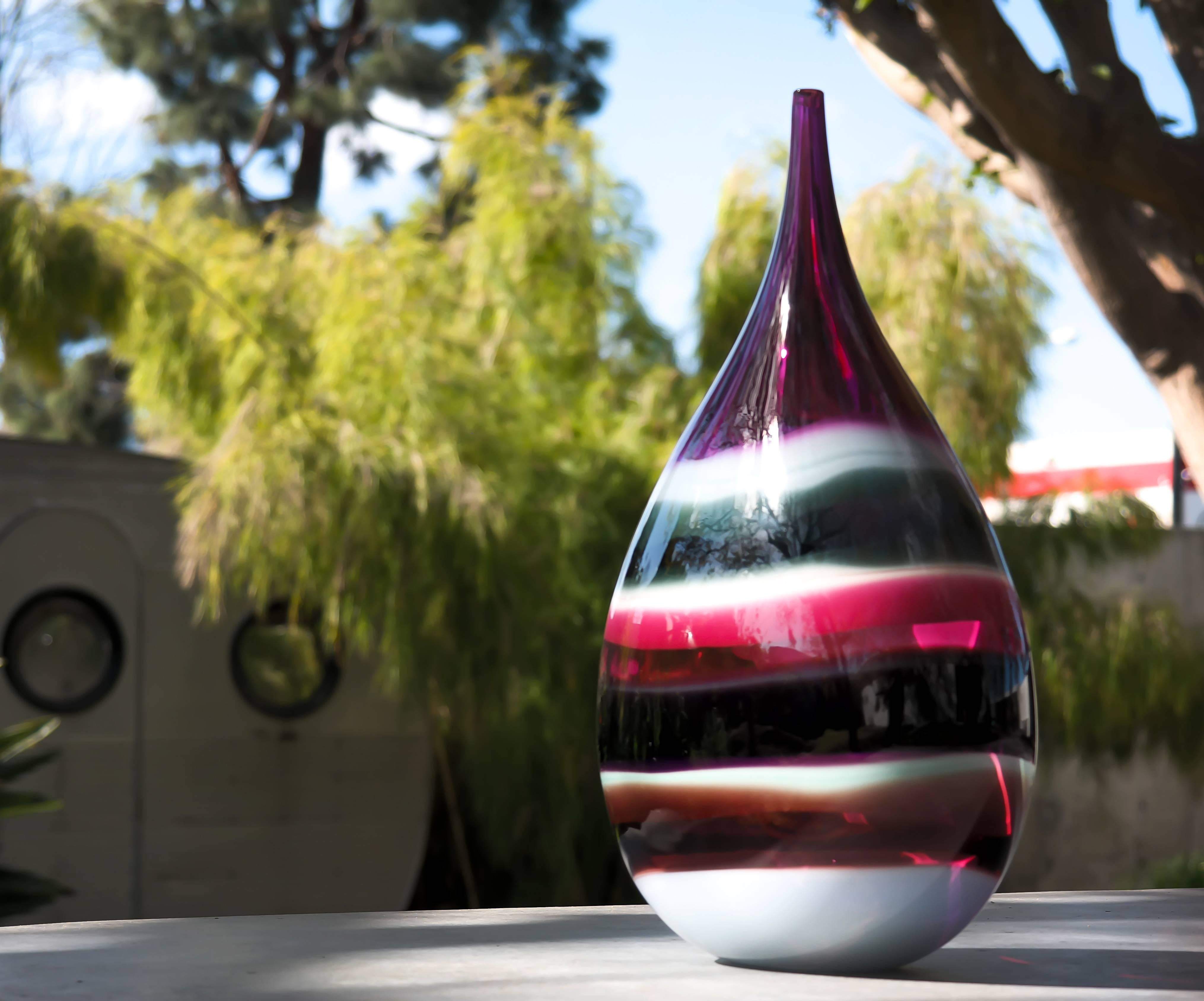 This striking hand blown glass vase draws inspiration from the rich hues and undulating topography of Southern California. Alternating layers of opaque and transparent colors are applied to clear glass. Overlaps create opportunities for new colors