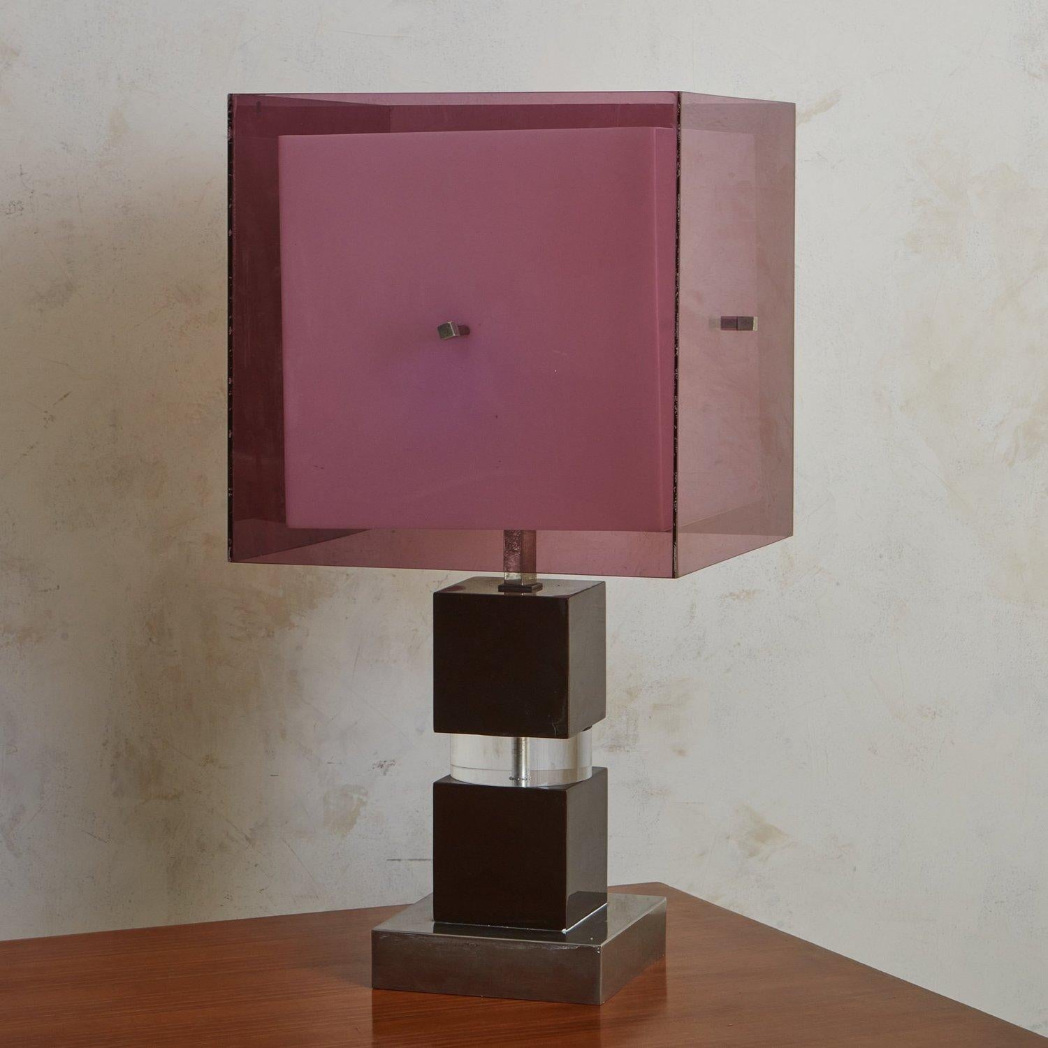 A 1970s Italian table lamp attributed to Romeo Rega. This lamp features a captivating purple lucite box shade with decorative metal cube hardware on each side. A smaller white acrylic shade floats within it. This lamp has a sculptural lucite +