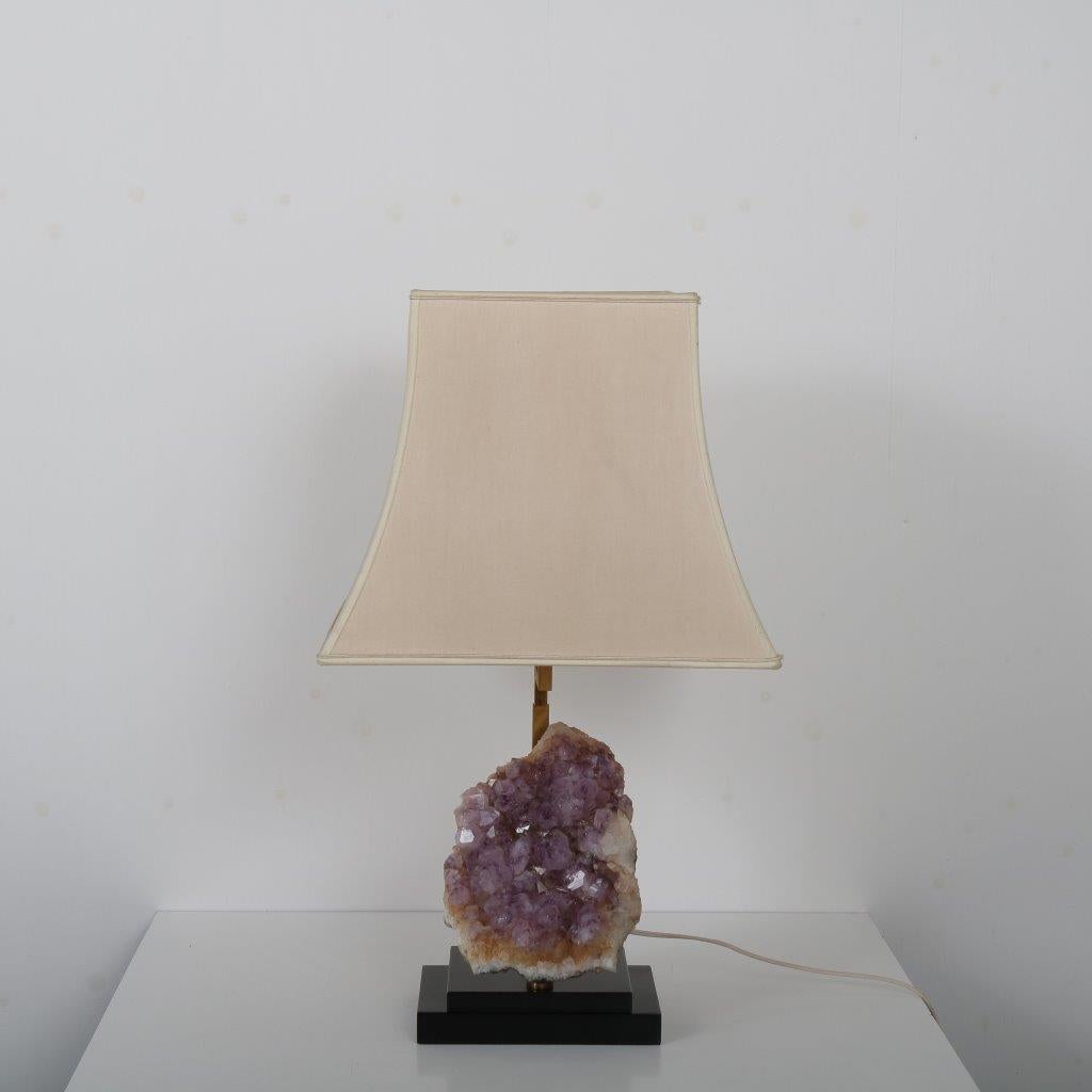 A rare table lamp with beautiful large Amethyst core, in the style of Willy Daro, manufactured in Belgium around 1970.

The lamp has a beautiful black with brass base, holding a beige fabric hood with a curved trapezium shape. The true eye-catcher