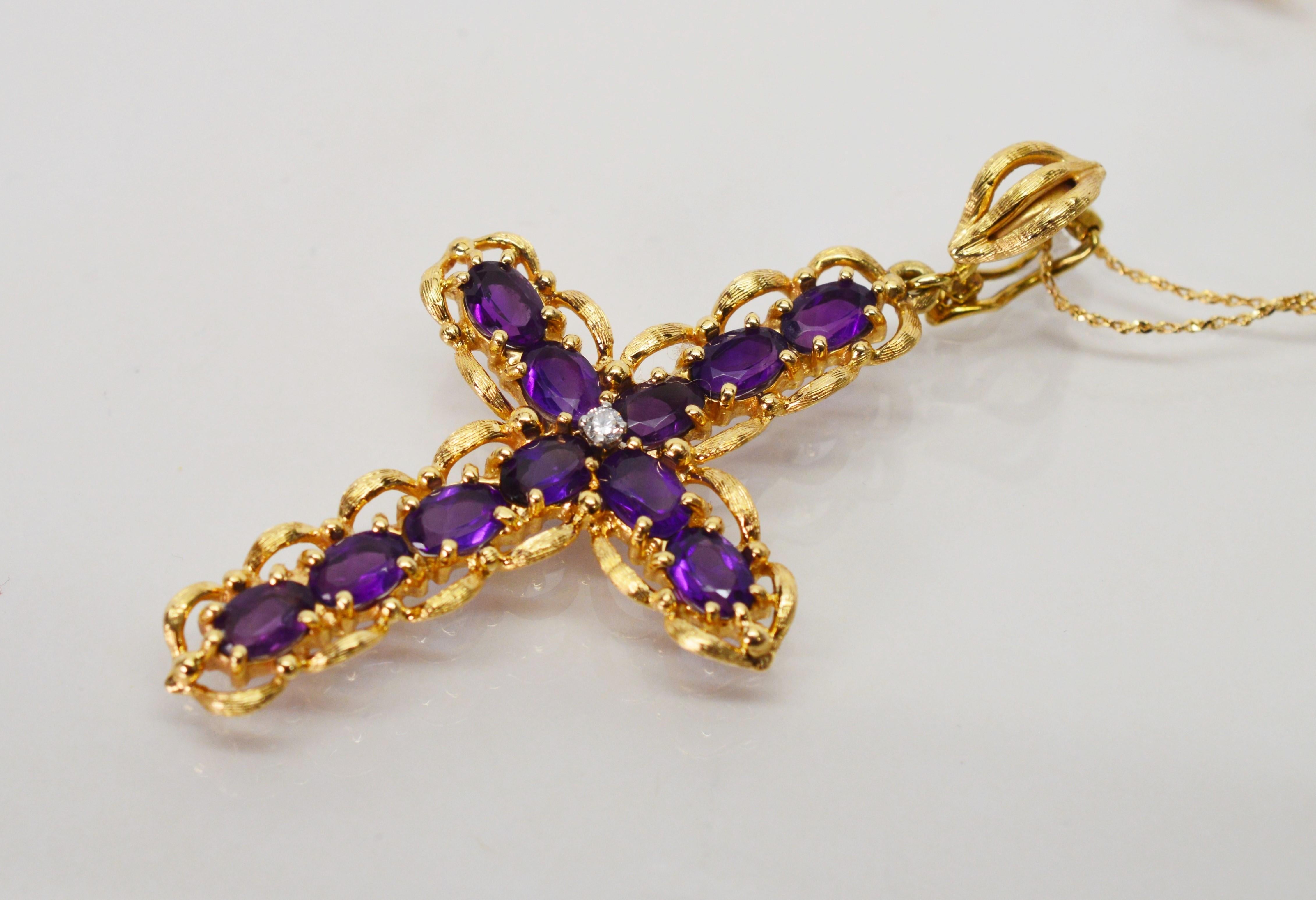 Nearly five carats of velvety purple amethyst gemstones and ribbons of fourteen karat yellow gold shaped this striking cross pendant with .02 carat center diamond accent. On an eighteen inch chain yellow gold chain, the pendant is fitted with an