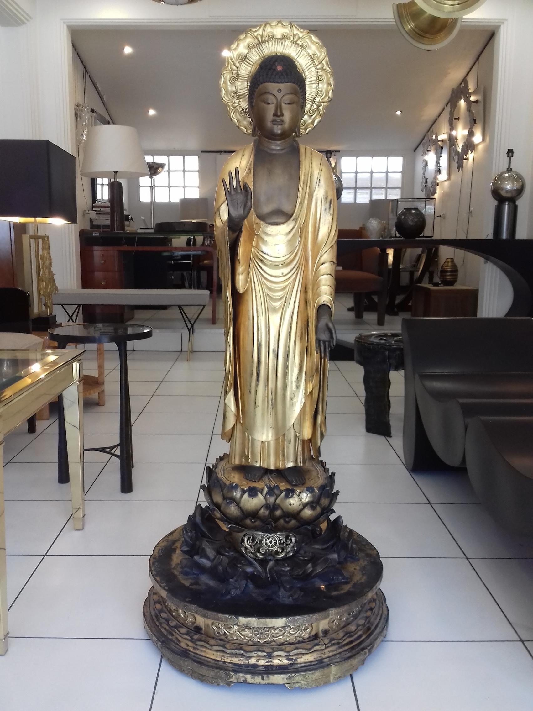 Fantastic Amida Buddha in gold lacquered wood, standing, the left foot slightly forward, on a lotus-shaped base, placed on a round base, in front of a halo formed by a fruit of lotus, the right hand in vitarka mudra (gesture of argumentation). Eyes