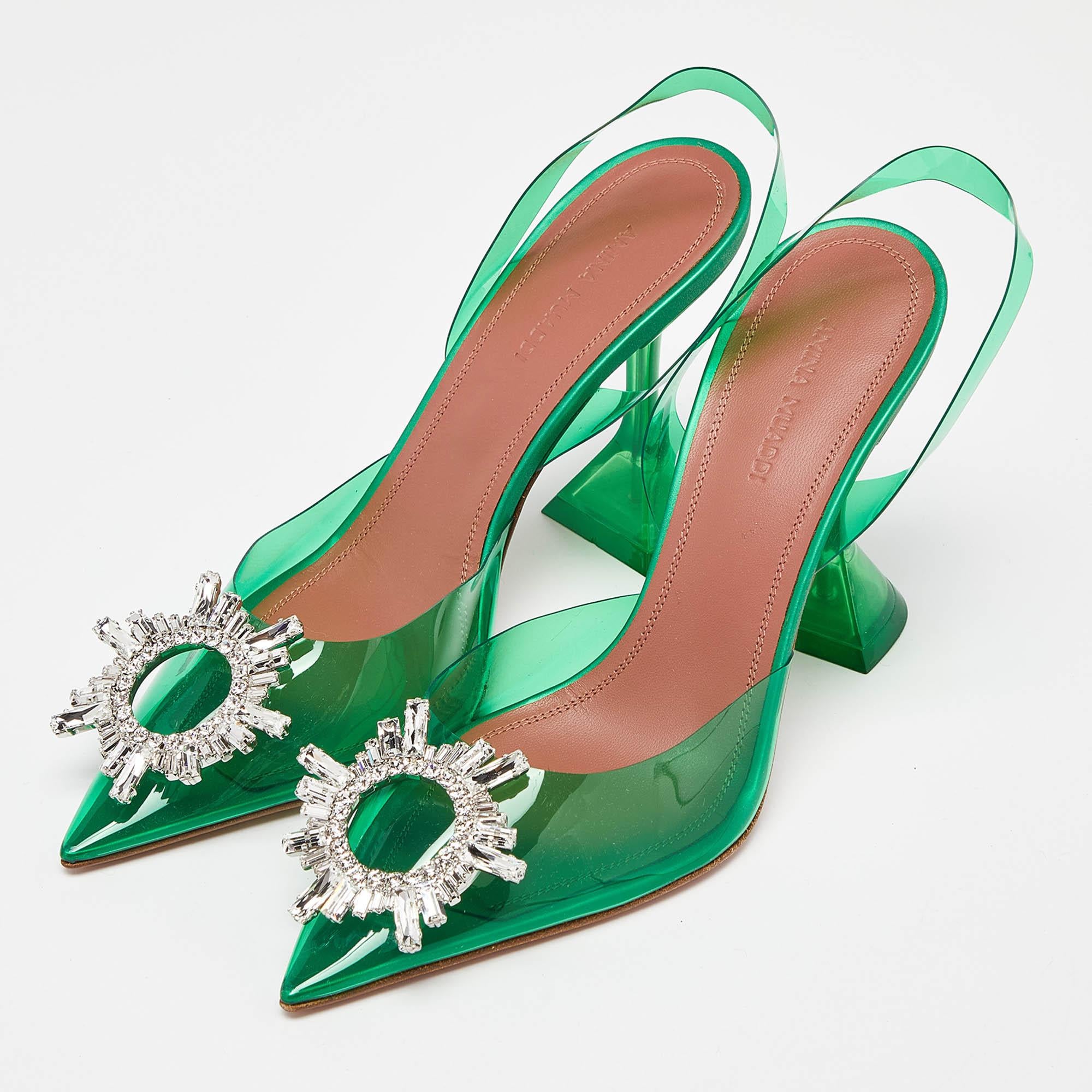The Amina Muaddi Begum pumps are striking high-heeled shoes. They feature transparent green PVC uppers, a pointed toe, and a sculpted heel with a signature flared design. These pumps exude modern elegance, combining transparency with a bold pop of