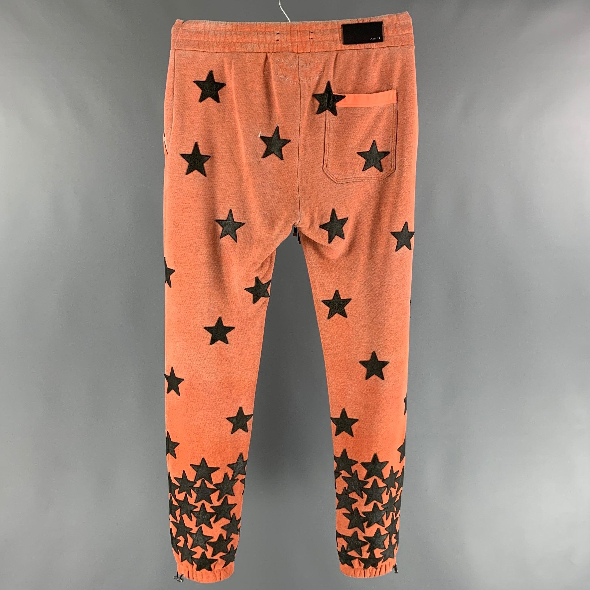 AMIRI sweatpants comes in an orange distress looking
 cotton french terry featuring leather black stars applique, zipper pockets, drawstring, cuffed legs, and an elastic waistband. Very Good Pre-Owned Condition. Minor pull around stars. As-Is.