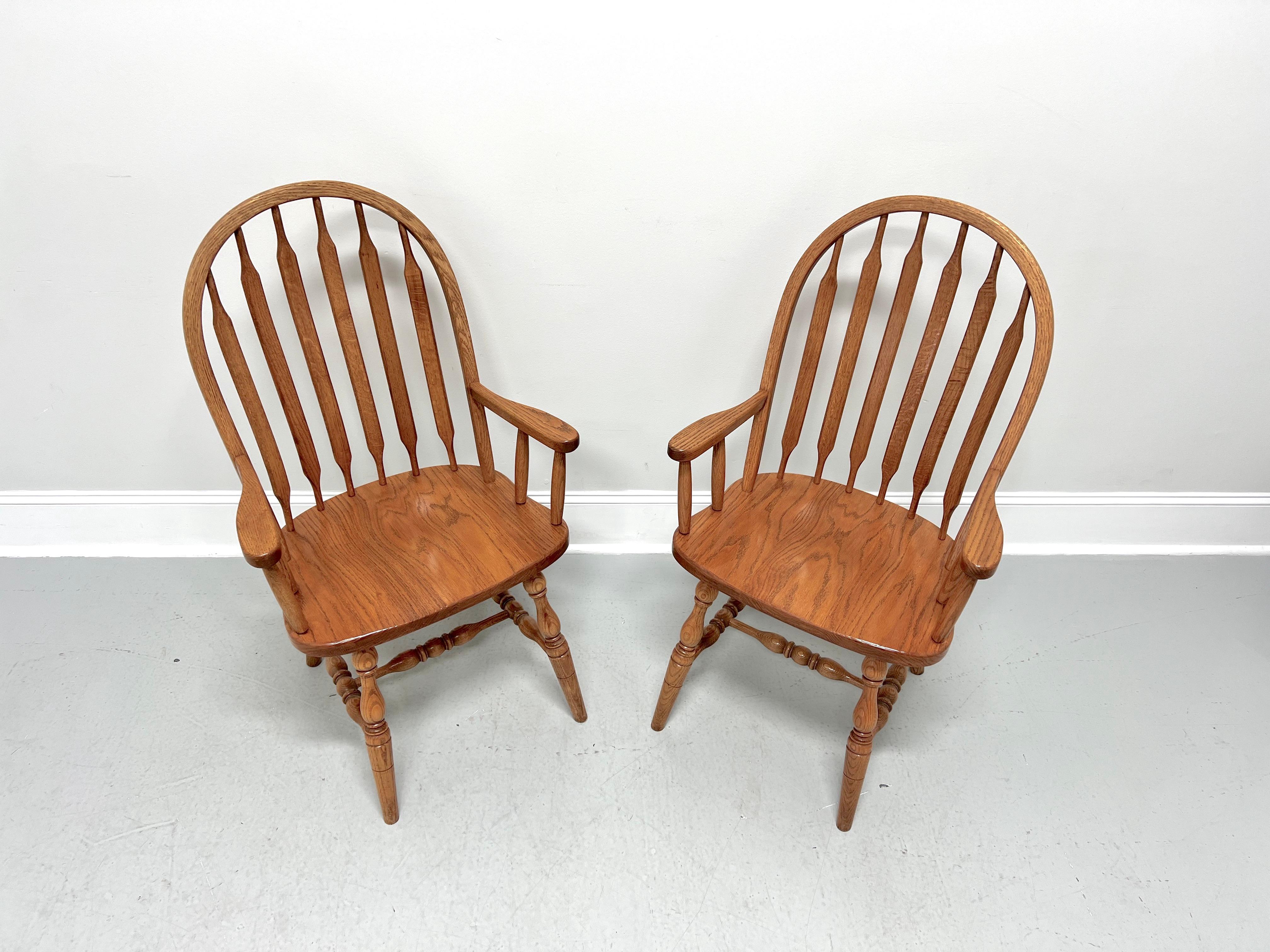A pair of handcrafted Windsor dining armchairs in the Rockford style by Amish craftsmen. Solid oak, bowback, cattail spindles, straight carved arms with spindle supports, solid seat, turned legs, and turned stretchers.  Made in the USA, in the late