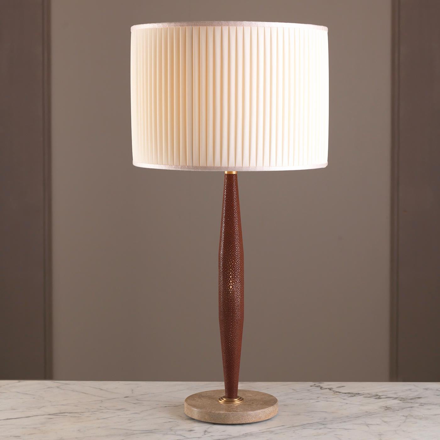 This timeless table lamp is designed by Ciarmoli Queda Studio and features a round Travertino marble base with a vertical stem tapered on both sides completely upholstered in stingray skin with top and bottom accents in brass. The drum-shaped shade