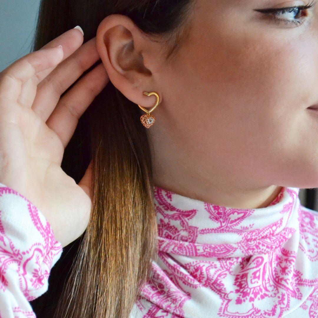 These exquisite earrings showcase a distinctive design that merges elegance with a modern twist. Featuring a heart-shaped outline earring, they dangle gracefully with a unique, 3D-like heart charm that captures attention.

The charm is adorned with