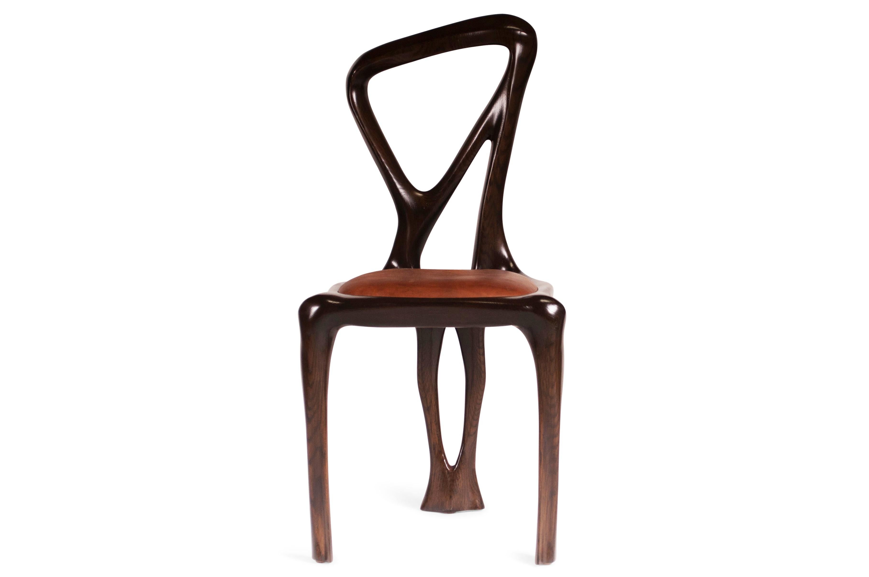 Chaise de salle à manger conçue par Amorph en bois de frêne massif et cuir. Il est teinté noyer foncé.
Dimension : 38