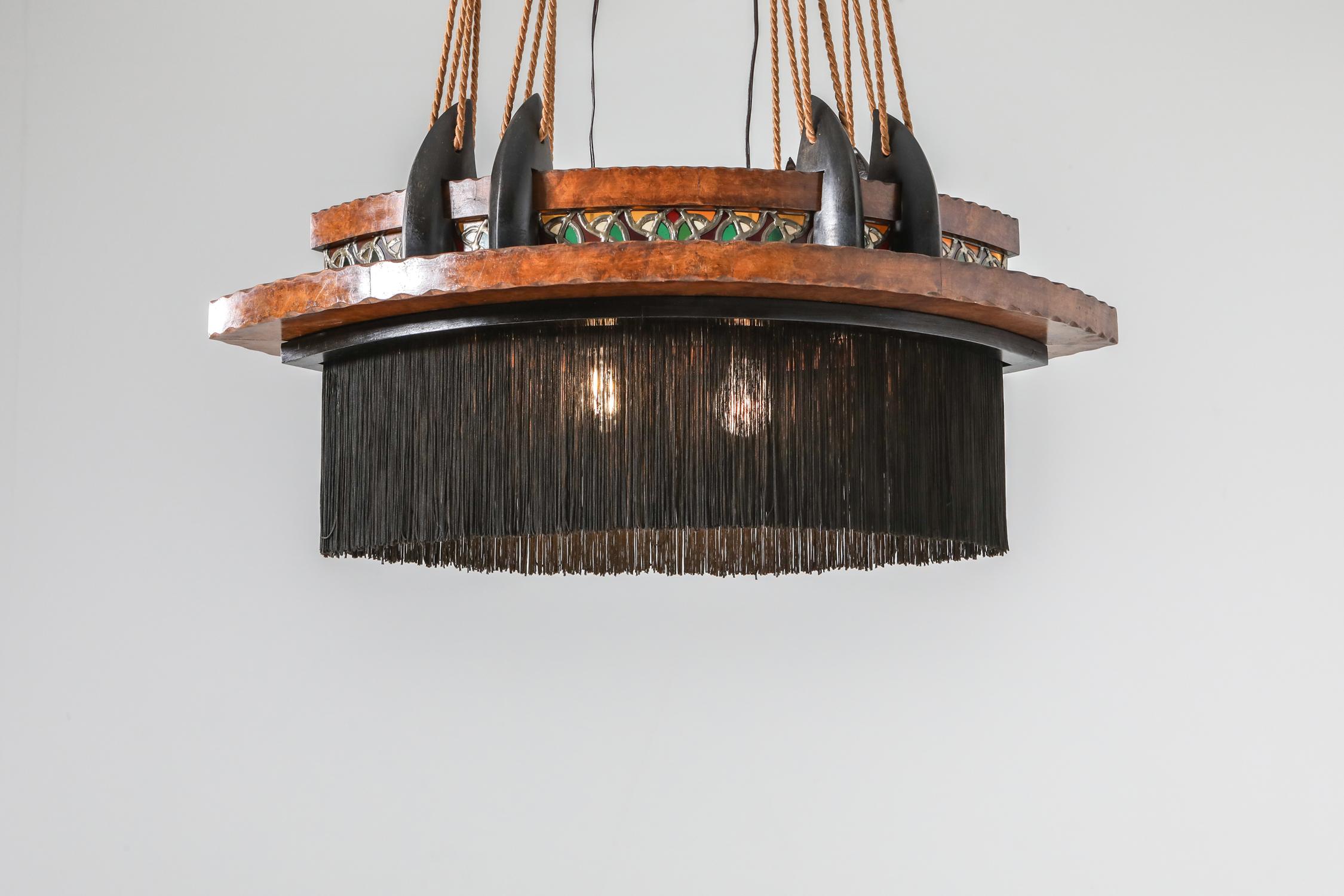 Dutch Art Deco era chandelier, Amsterdam School, 1920s

Expressionist piece with exuberant details like the multicolored glass in lead, the silk fringes, the carved fruitwood and the ebonized and carved details.
The chandelier also has the almond