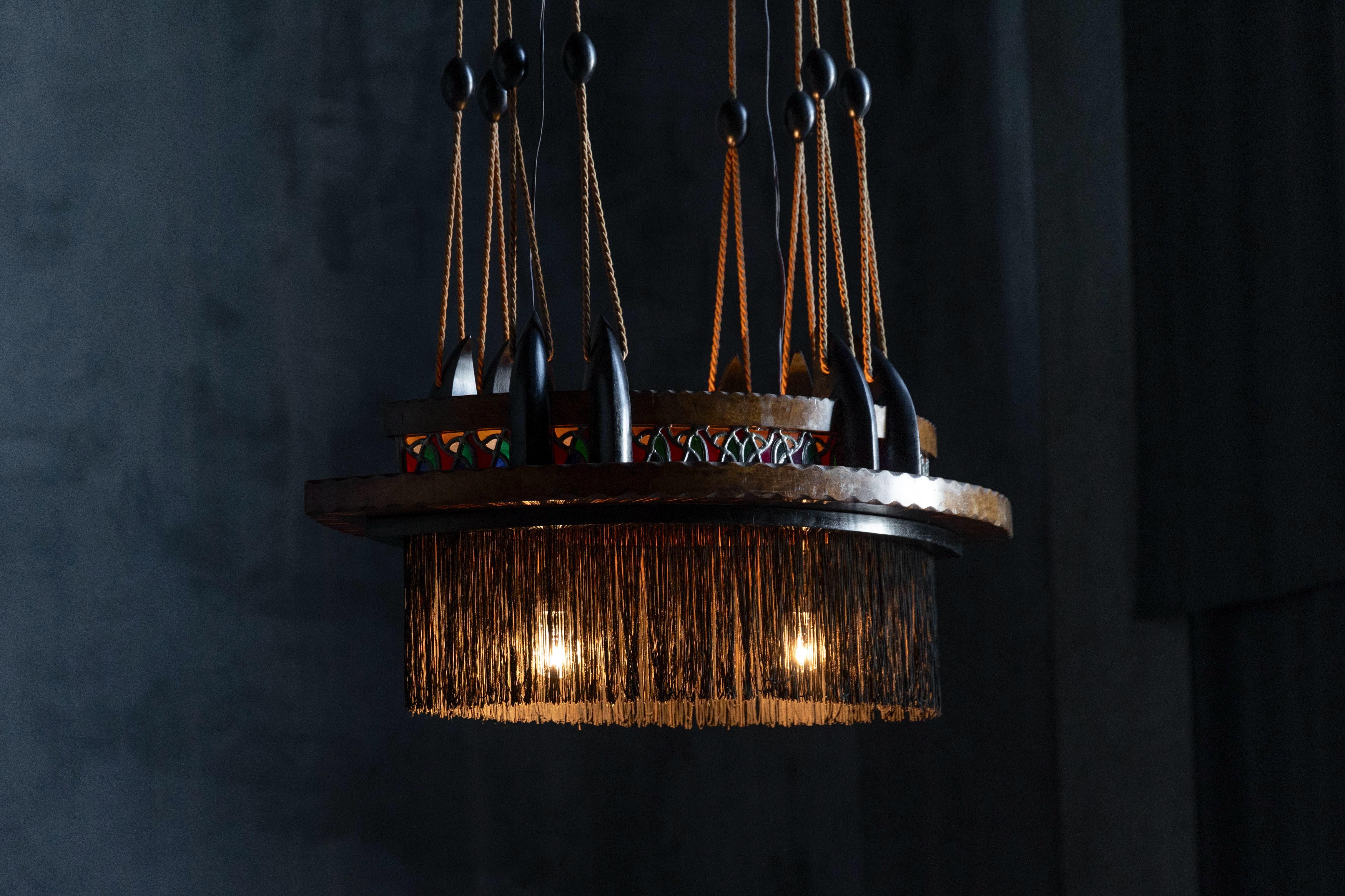 A striking Dutch Art Deco chandelier from the 1920s, crafted in the expressive Amsterdam School style. This piece features hand-carved fruitwood paired with ebonized accents, delicate silk fringes, and vibrant stained glass in lead. The
