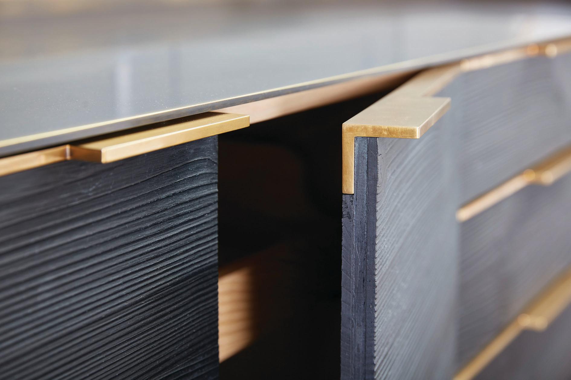 Un cadre en bronze foncé avec des reflets dorés crée la structure d'une armoire audacieuse fabriquée avec des portes et des tiroirs en pin calciné. Le processus de réalisation de la finition des faces de l'armoire met en valeur le caractère naturel
