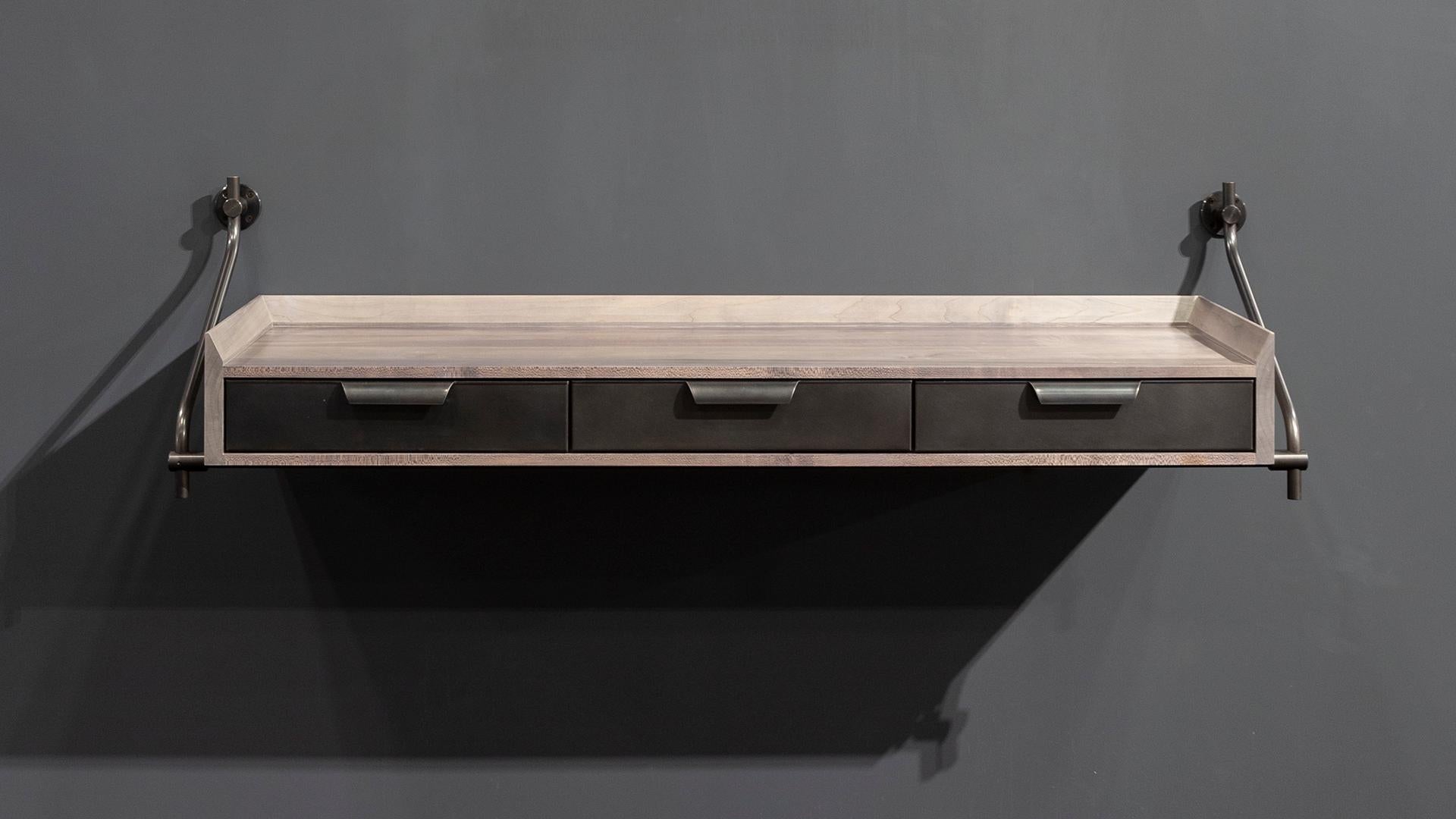 La console murale en érable tendre patiné d'Amuneal utilise notre système traditionnel d'étagères de collection pour soutenir ce meuble à trois tiroirs entouré d'un bord de couteau surélevé. L'échelle de l'unité et son design flottant unique en font
