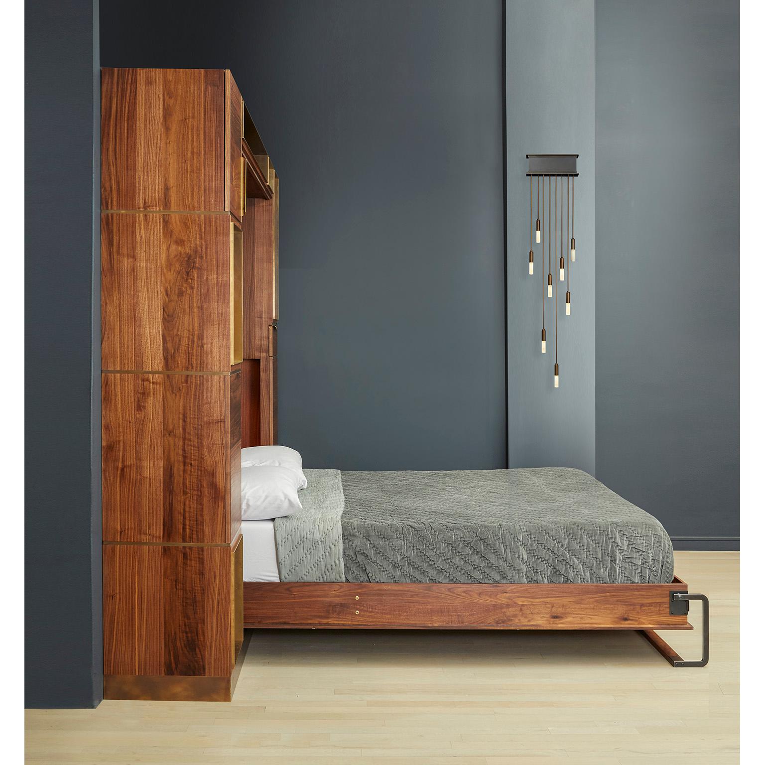 Das Bett von Amuneal, das sich wie ein eingebautes Möbelstück anfühlt, verbirgt eine Queensize-Matratze hinter Paneelen aus versilbertem Nussbaumholz mit Intarsien aus oxidierter Bronze. Bei geschlossenem Bett schaffen die Nussbaum- und