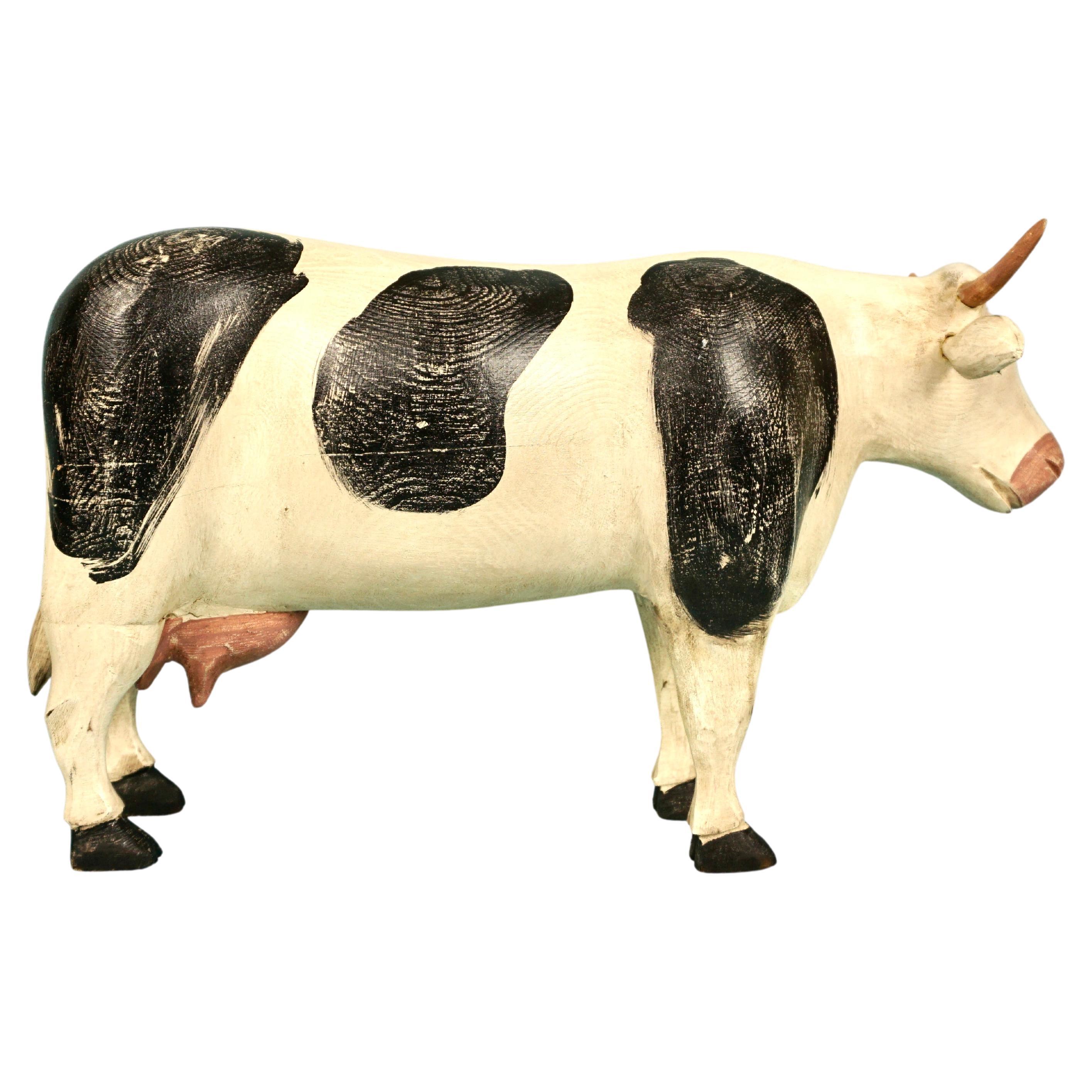 A charming full-bodied carved wooden Holstein cow with an bemused look on her face, the well-fed animal possessing horns, signed on the belly BHC '89. Our girl has protruding ears and pronounced black and white markings with a long distinctive tail.