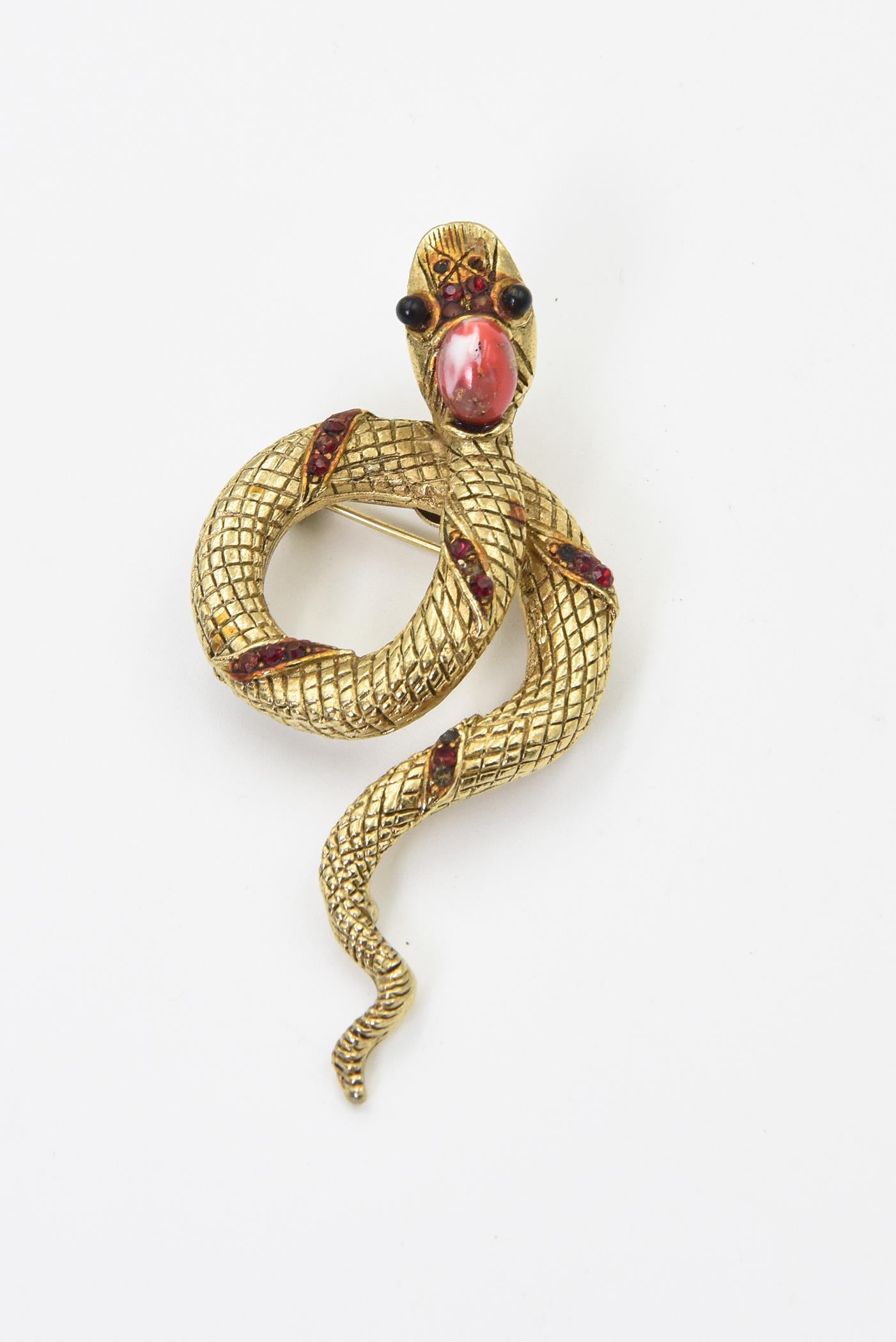 Adorable smiling or maybe hungry gold tone snake brooch featuring a highly stylized snake with rhinestone red bands and black beady eyes.