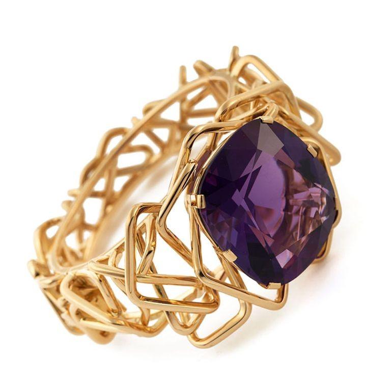 A stunning amethyst and gold statement bangle by Amy Burton, the bangle centred on a beautiful antique cushion-cut amethyst of rich purple hue weighing 123.70cts, claw set and surrounded by an asymmetric, three dimensional, sculptural maze of 18ct