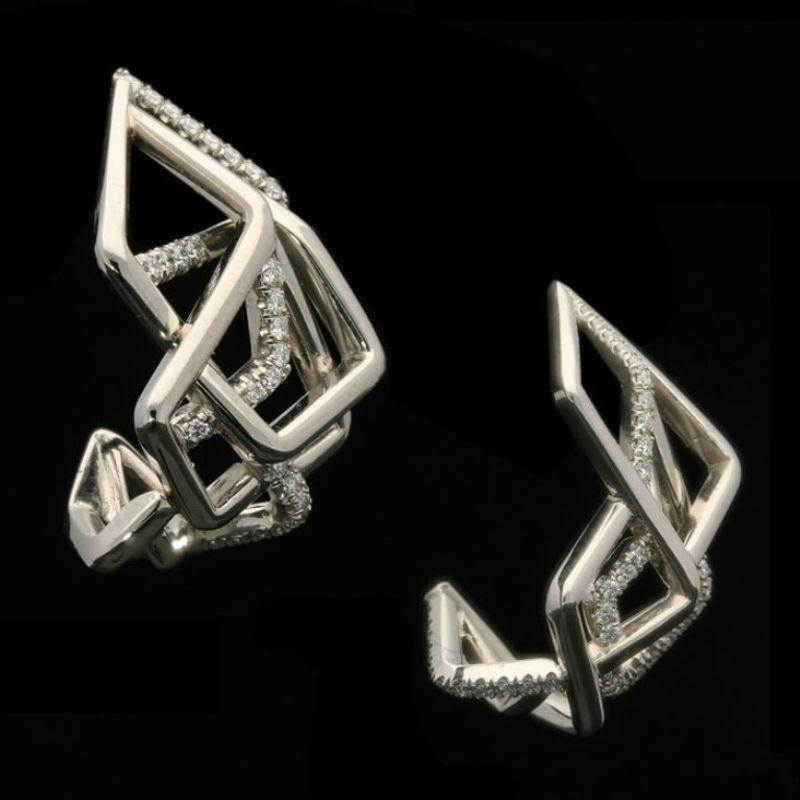 A beautiful pair of Disorient platinum and diamond earrings by Amy Burton, the elongated open hoops finely hand crafted and of sculptural asymmetric openwork design with three dimensional overlapping angular forms partly set with round brilliant cut